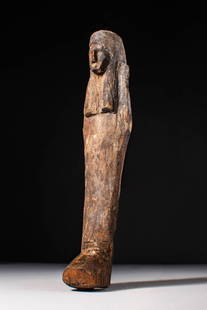 EGYPTIAN WOODEN USHABTI: New Kingdom, Ca. 1550 - 1069 BC. A wooden ushabti figure depicted standing with hands placed on the chest and wearing a tripartite wig. Its side lappets fall over the shoulders and extend down the upp