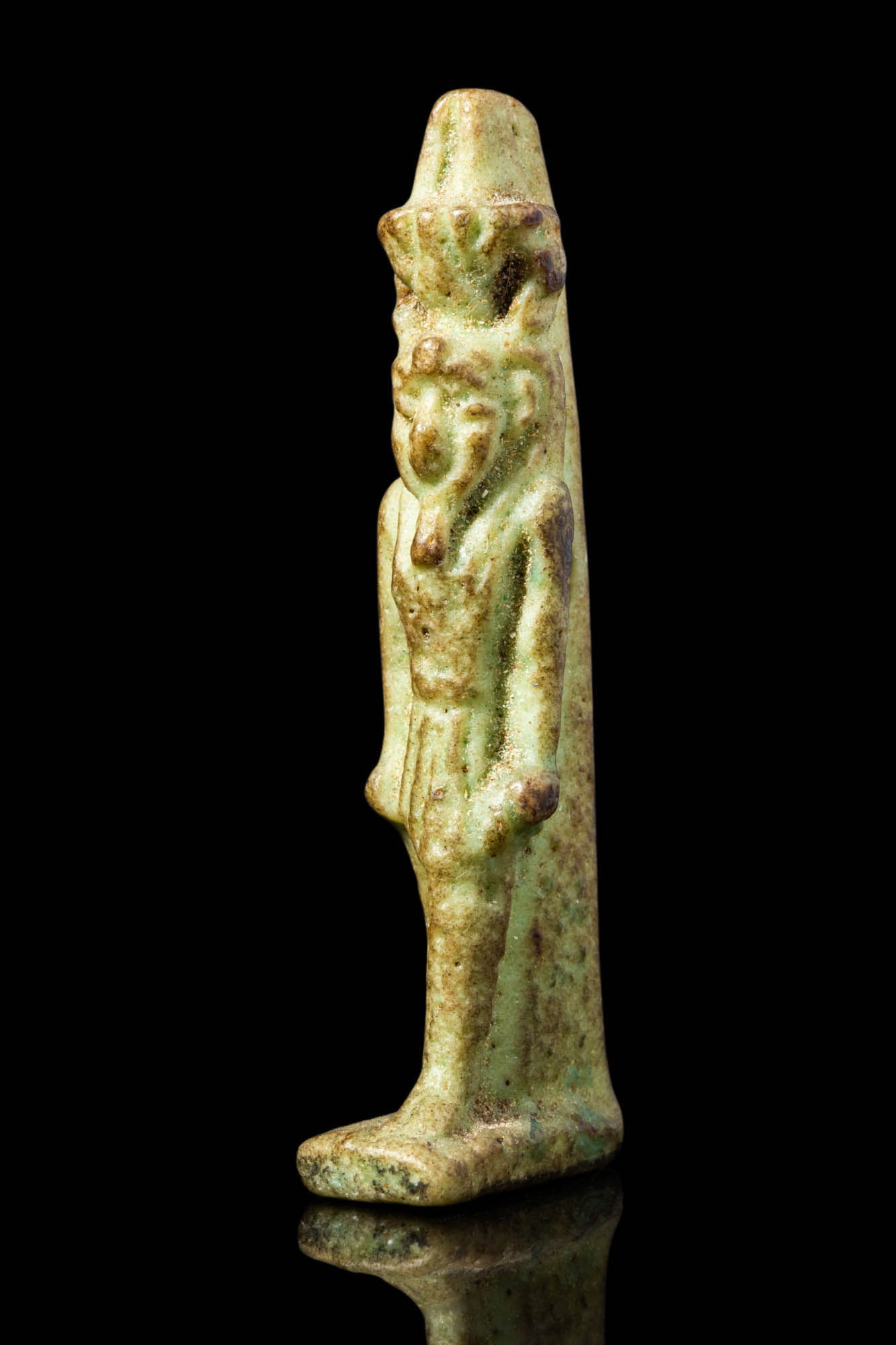 EGYPTIAN FAIENCE NEFERTEM AMULET: Late Period, Ca. 664 - 332 BC. A faience amulet depicting Nefertem in a striding pose with his left leg forward. He wears a short kilt and a tall lotus headdress. His arms are held straight at his sid