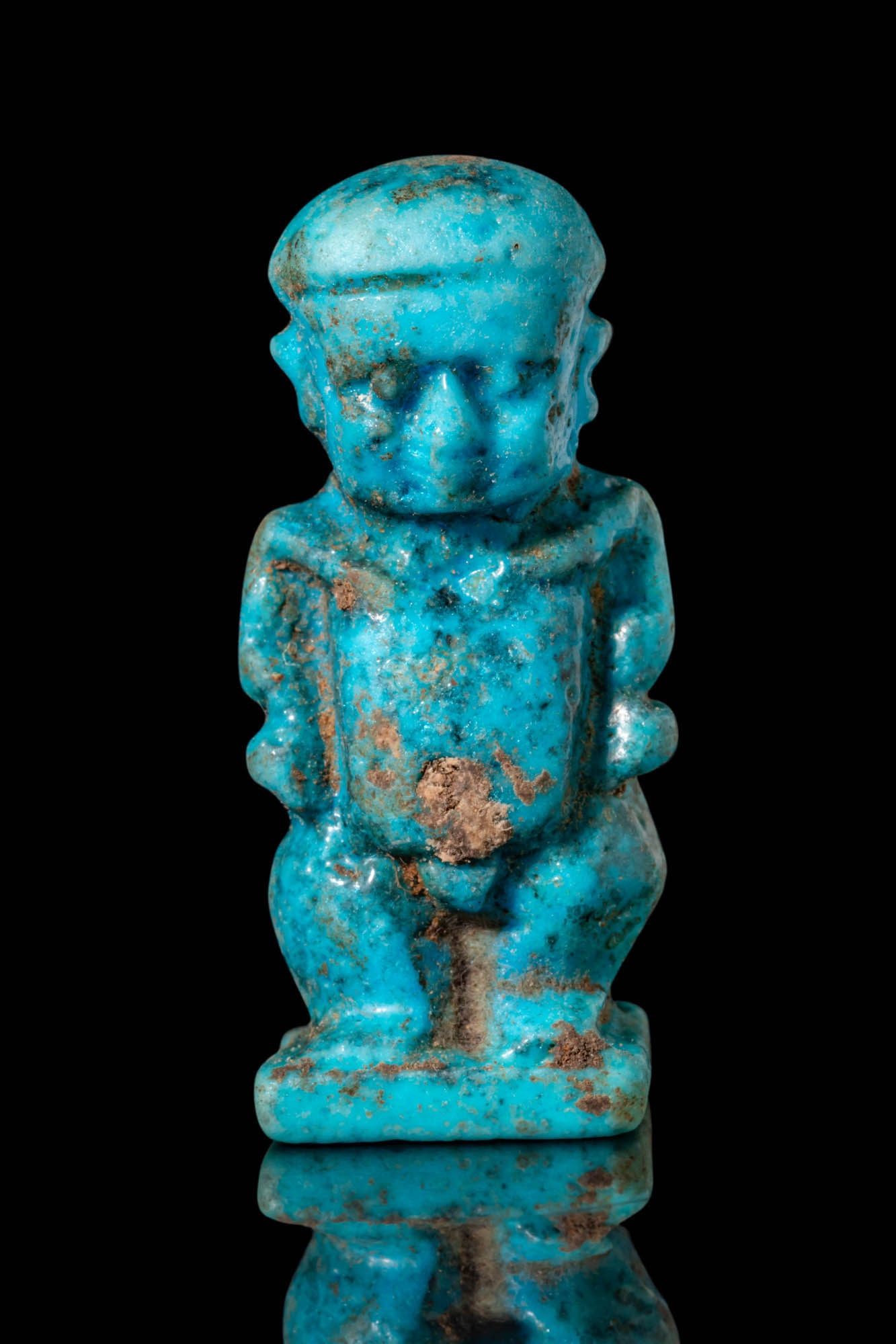 EGYPTIAN FAIENCE PATAIKOS AMULET: Third Intermediate Period to Late Period, Ca. 1069 - 332 BC. A blue faience amulet of Pataikos depicted as a squat, nude figure standing on a rectangular base. The rounded head is adorned with a plain