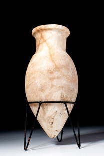 EGYPTIAN ALABASTER VESSEL: Ca. 2900 - 2200 BC. A slender alabaster vessel with an elongated piriform body tapering to a pointed base and a short cylindrical neck widening into a rounded, everted rim. The stone presents pale cre