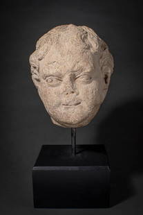 ROMAN MARBLE HEAD OF A PUTTO: Ca. AD 250 - 400 A Roman marble head of a Putto sculpted from a single piece of marble. The face has sensitively rendered features, including heavily-lidded eyes with drilled pupils beneath a thin bro
