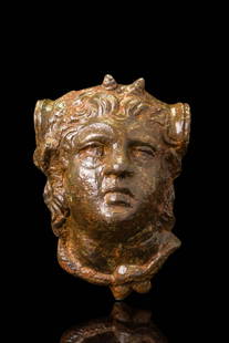 ROMAN BRONZE APPLIQUE OF A YOUNG SATYR: Ca. AD 200. A finely modelled head of a youthful satyr with rounded cheeks, full lips, and wide-set eyes beneath arched brows. Thick, wavy hair is swept back, with a pair of small horns emerging from