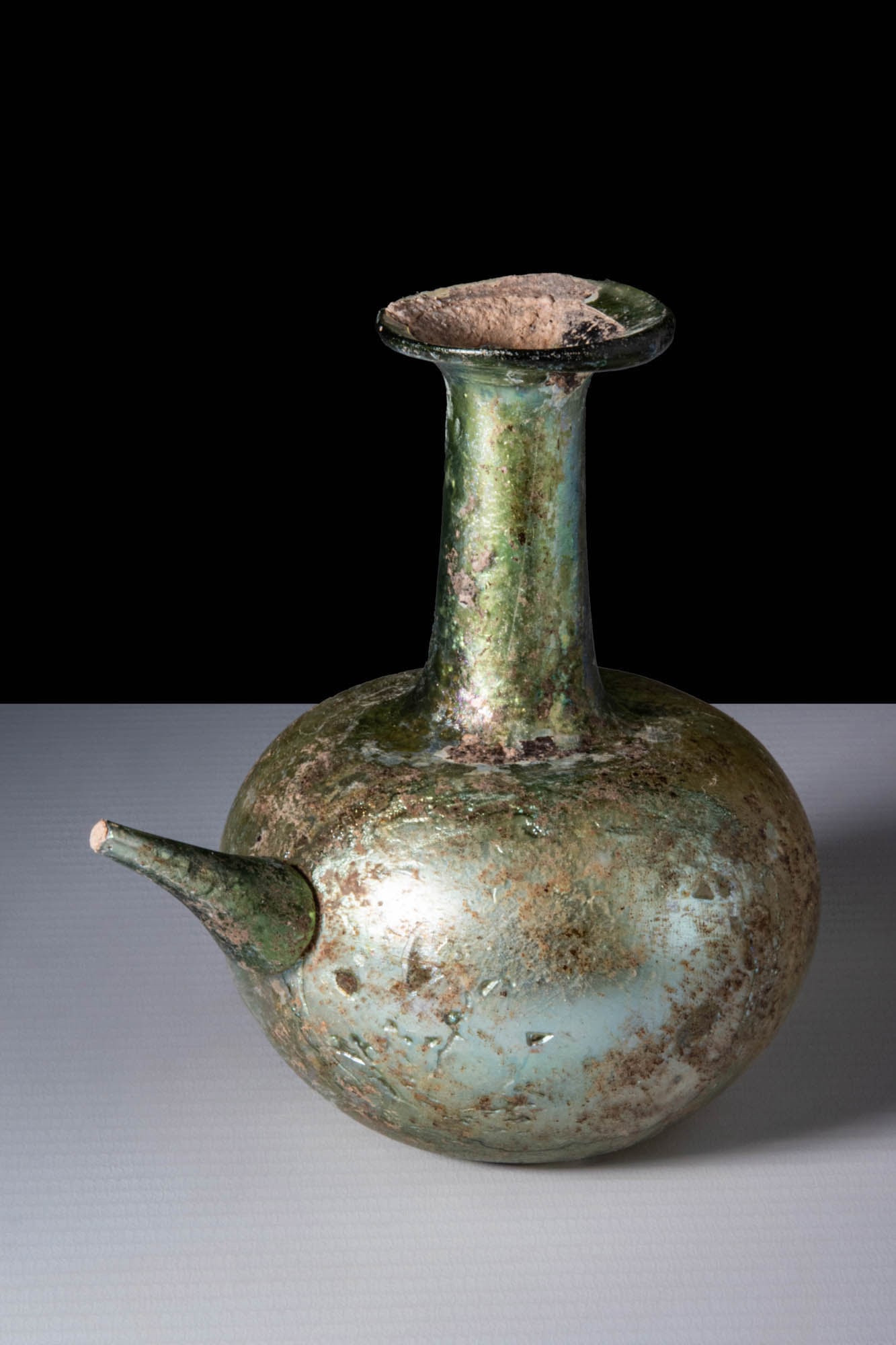 SUPERB ROMAN GLASS INFUNDIBULUM (LAMP FILLER): Ca. AD 100 - 200. An olive-green, free-blown glass flask with an apple-shaped lower body and a long, cylindrical neck that ends in a slightly flared mouth with a thick, pronounced rim. The base is fla