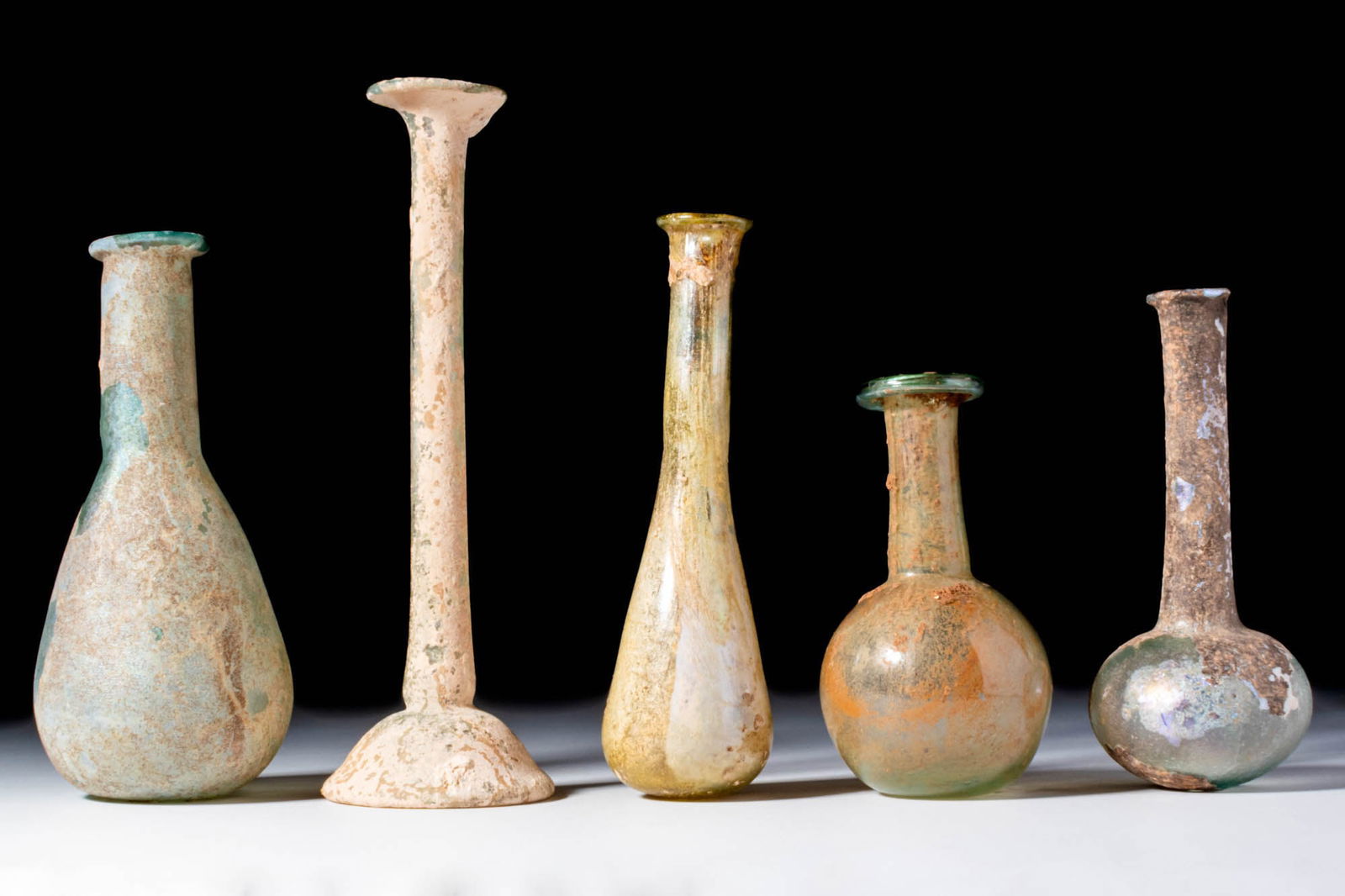 COLLECTION OF ROMAN GLASS UNGUENTARIA: Ca. AD 1 - 300. A collection of five glass unguentaria with varying proportions of necks and rounded or pear-shaped bodies. The rims are mostly folded. The glass shows a range of pale green, blue and