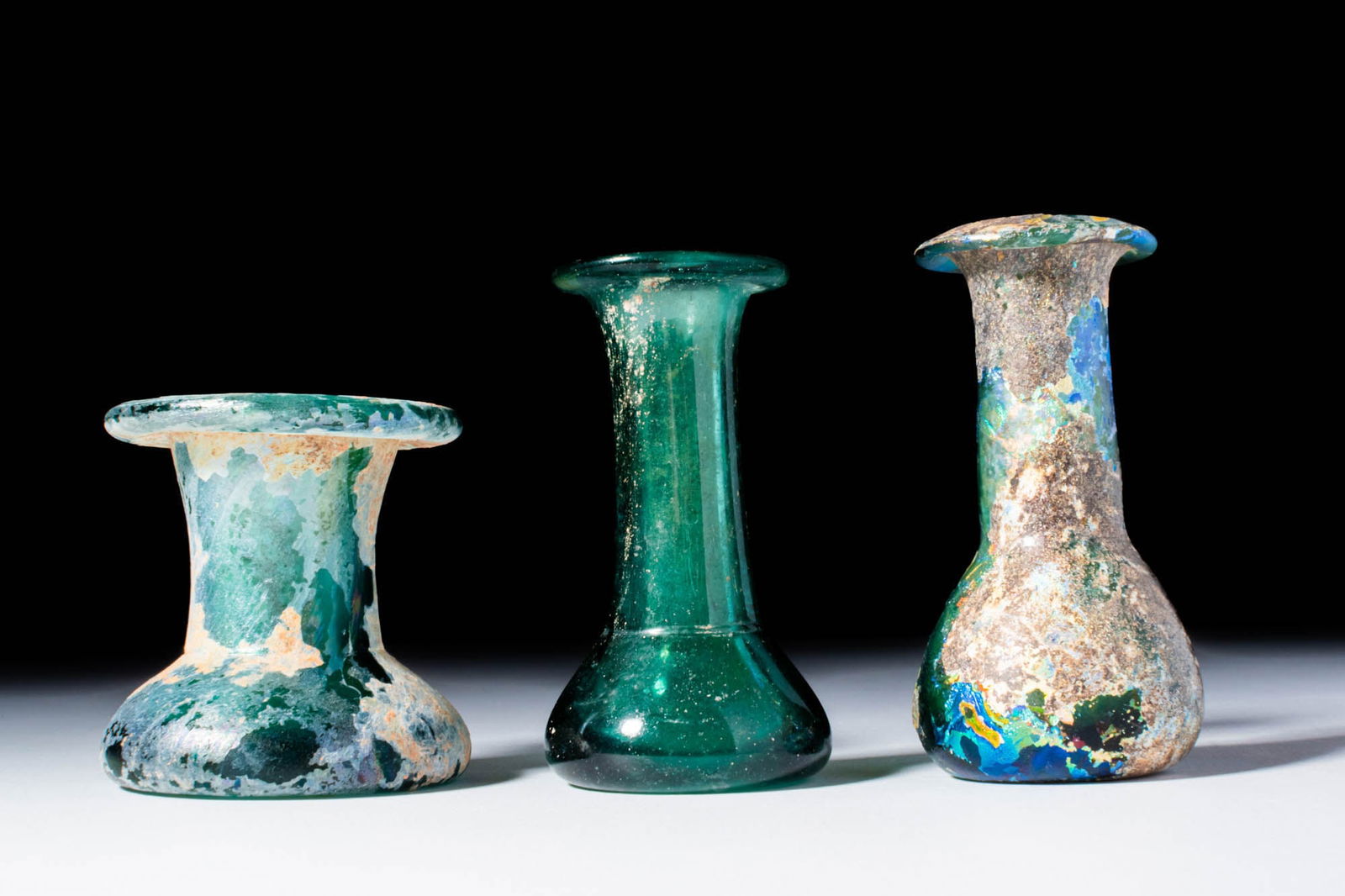 COLLECTION OF ROMAN UNGUENTARIA: Ca. AD 1 - 300. A trio of dark green glass spool-shaped unguentaria with thick, rounded rims, cylindrical necks, and domed bases. For similar see: C. S. Lightfoot, The Cesnola Collection of Cypriot Ar
