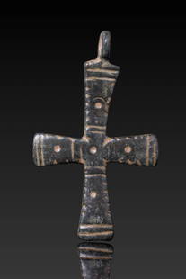 BYZANTINE BRONZE CROSS PENDANT: Ca. AD 900 - 1100. A bronze cross pendant with flaring arms, each marked by a central circular indentation, framed by parallel lines and notched edges. A suspension loop is set above the upper arm.For