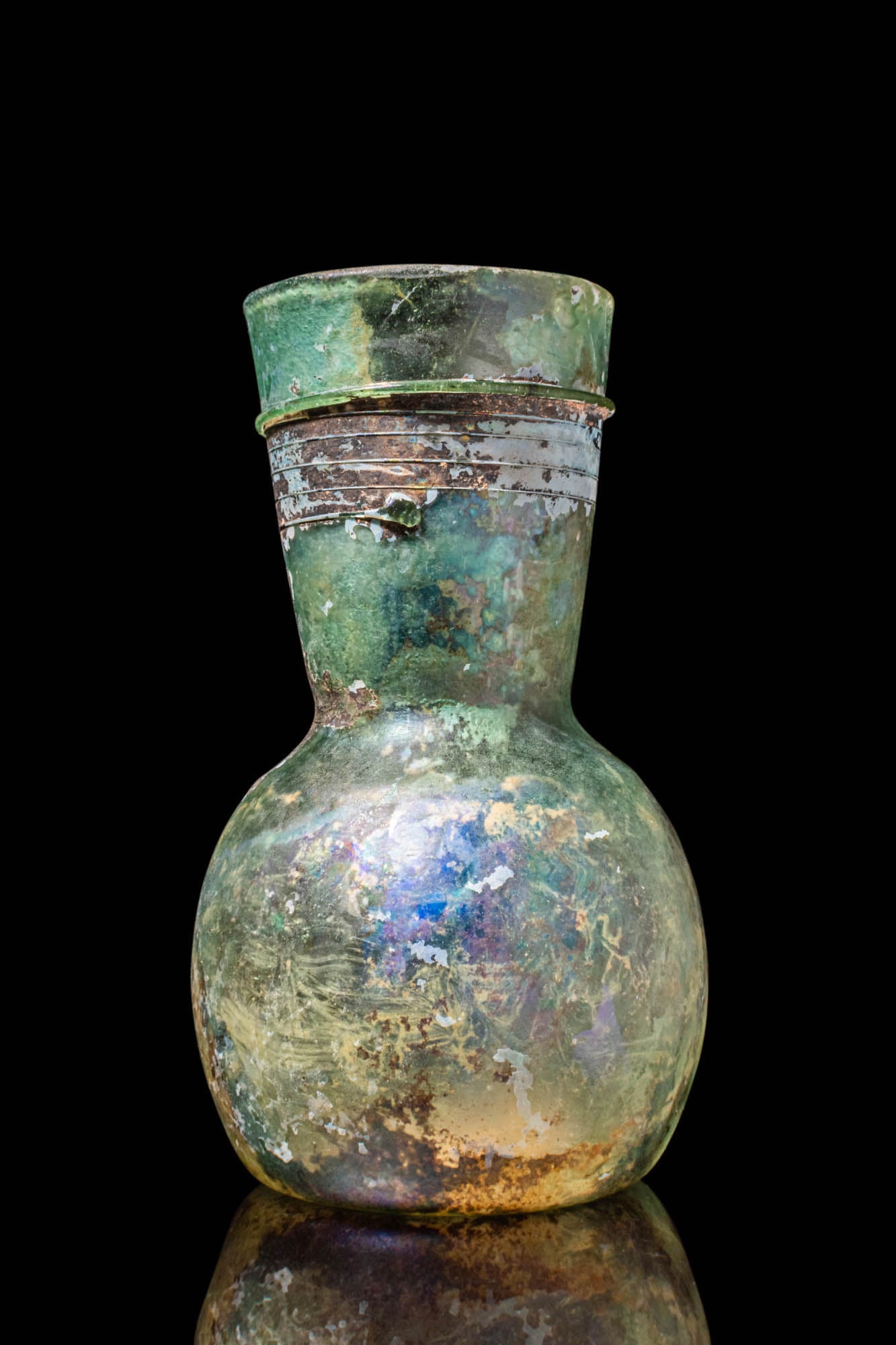 UMAYYAD GLASS BOTTLE: Ca. AD 900. A glass bottle with a bulbous body and a wide, funnel-shaped mouth with a rounded rim. Thin, horizontal bands of applied glass threads encircle the neck in closely spaced parallel lines. T