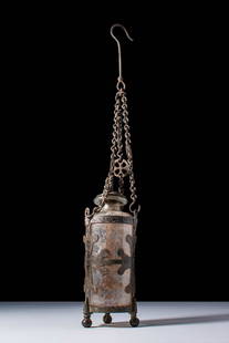 RARE BYZANTINE GLASS BOTTLE IN BRONZE OPENWORK SUSPENSION MOUNT: Ca. AD 500 - 700. A cylindrical glass bottle set within an openwork bronze mount, suspended by three chains joined at the top by a hook and converging through a pierced rosette terminal. The clear