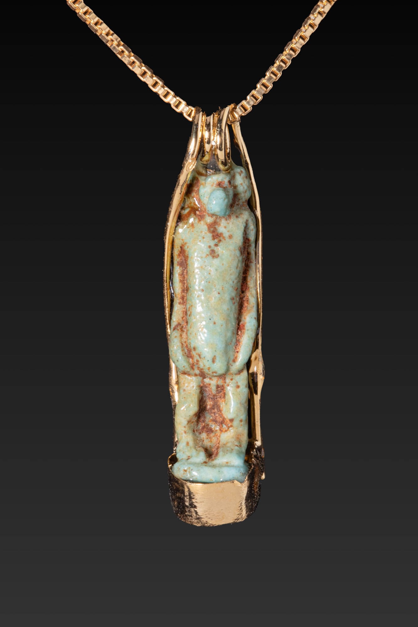 EGYPTIAN FAIENCE STANDING GOD AMULET IN GILDED SILVER PENDANT SETTING: Ca. 30 BC - AD 200. A faience amulet depicting a standing god with an animal head. The figure displays a hanging belly, arms placed along the sides, and parallel legs set together on an integral recta