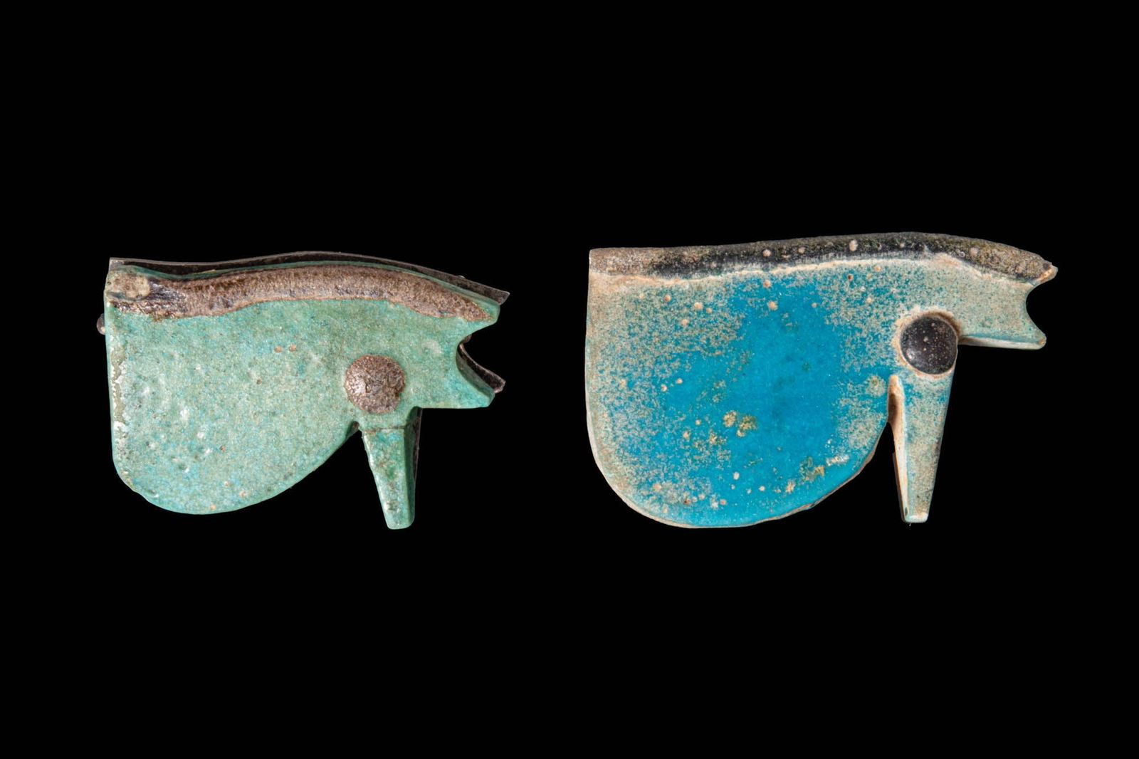 PAIR OF EGYPTIAN FAIENCE WEDJAT AMULETS: Third Intermediate Period, Ca. 1069 - 664 BC. A pair of faience wedjat amulets; each formed as a flat plaque with a raised dark brow band, a dark circular pupil, and a vertical projection beneath the