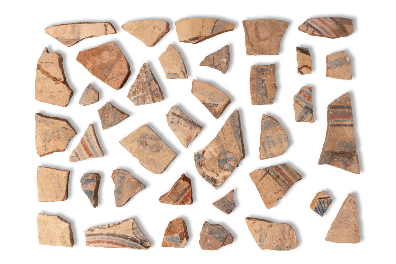 COLLECTION OF EGYPTIAN AMARNA PERIOD PAINTED JAR FRAGMENTS: Amarna Period, Ca. 1353 - 1336 BC. A collection of terracotta fragments with painted decoration in red, blue, and black on a light buff ground. The sherds preserve elements of radial rosettes, lotus f