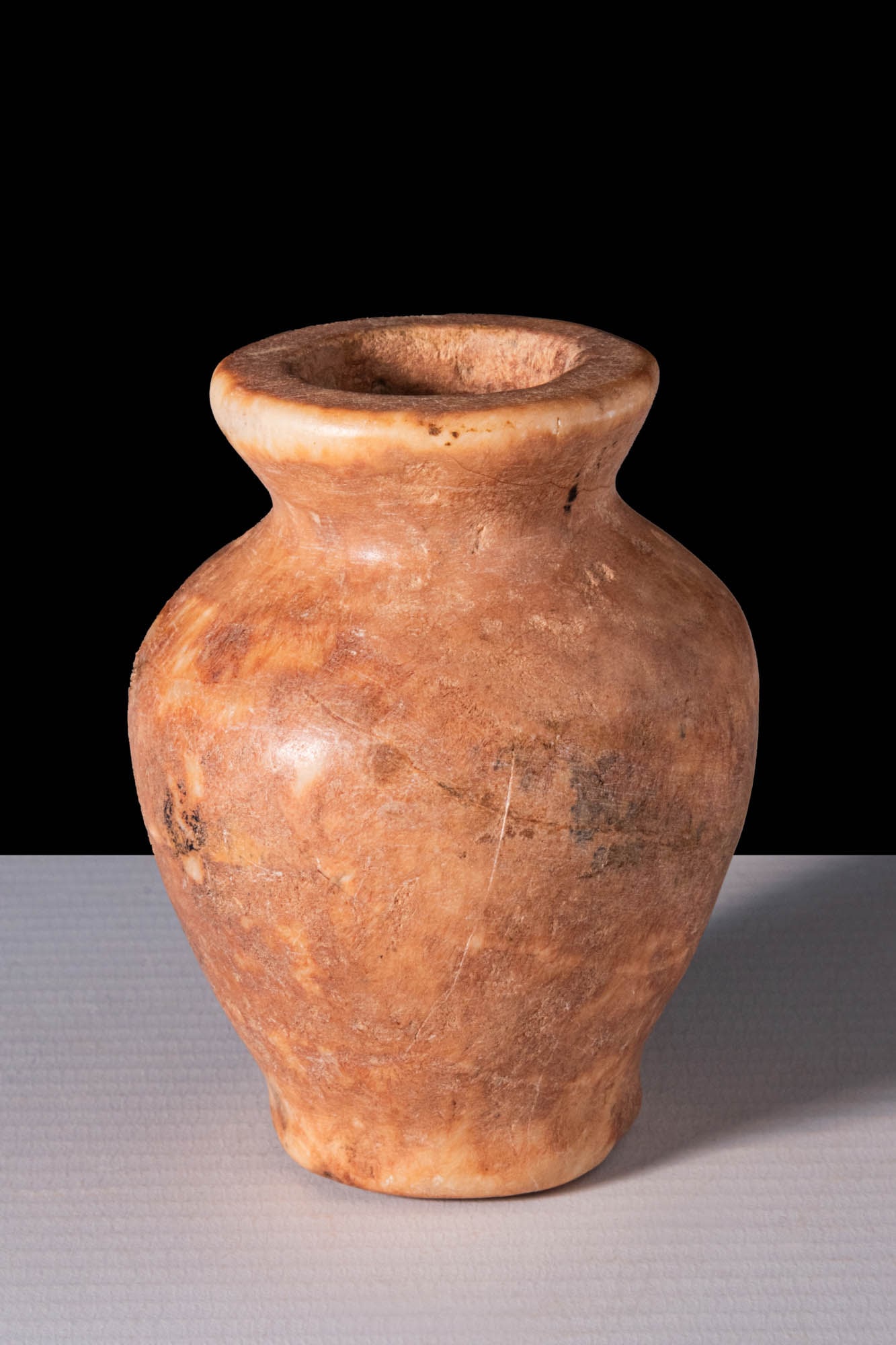 EGYPTIAN ALABASTER COSMETIC VESSEL: Middle Kingdom, Ca. 2055 - 1773 BC. An alabaster cosmetic vessel with a rounded body tapering towards a low foot and a short, concave neck flaring to a wide, flat rim.For similar see: Christie's, Live