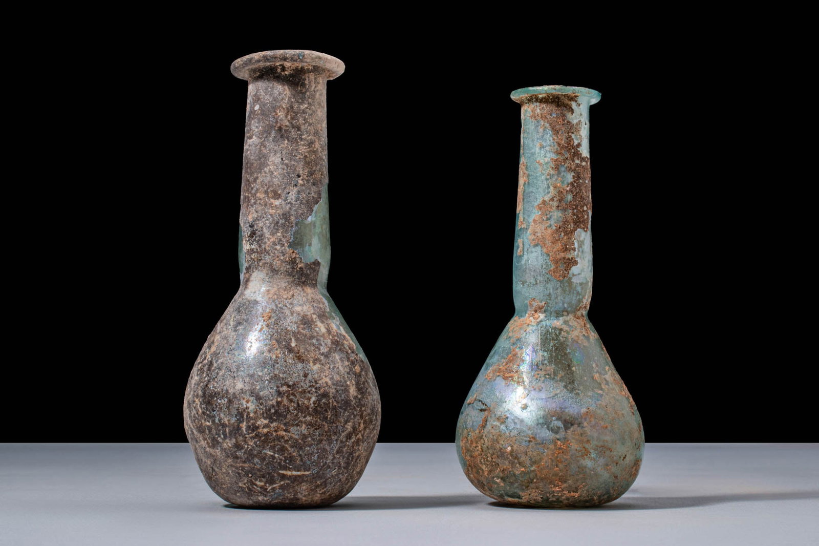 PAIR OF ROMAN GLASS BOTTLES: Ca. AD 1 - 200. A pair of pale blue-green glass bottles, each free-blown with a piriform body, a long cylindrical neck rising from a slight constriction, and a flared rim with a rounded lip.For simila