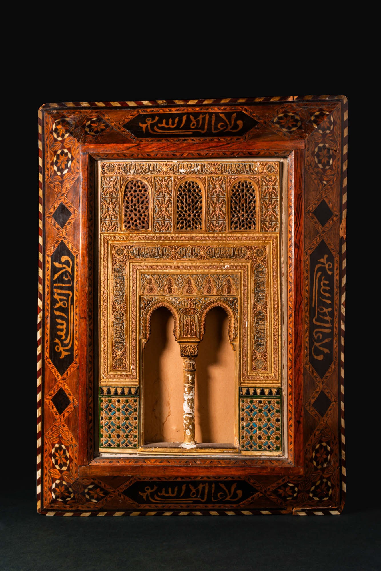 ISLAMIC INLAID WOODEN MODEL OF THE ALHAMBRA PALACE: Spain, Granada, Ca. end of 19th century AD. A modelled façade from the Alhambra Palace, Granada in carved stucco, polychromed and gilt, set as a deep niche with a twin cusped horseshoe arch supported