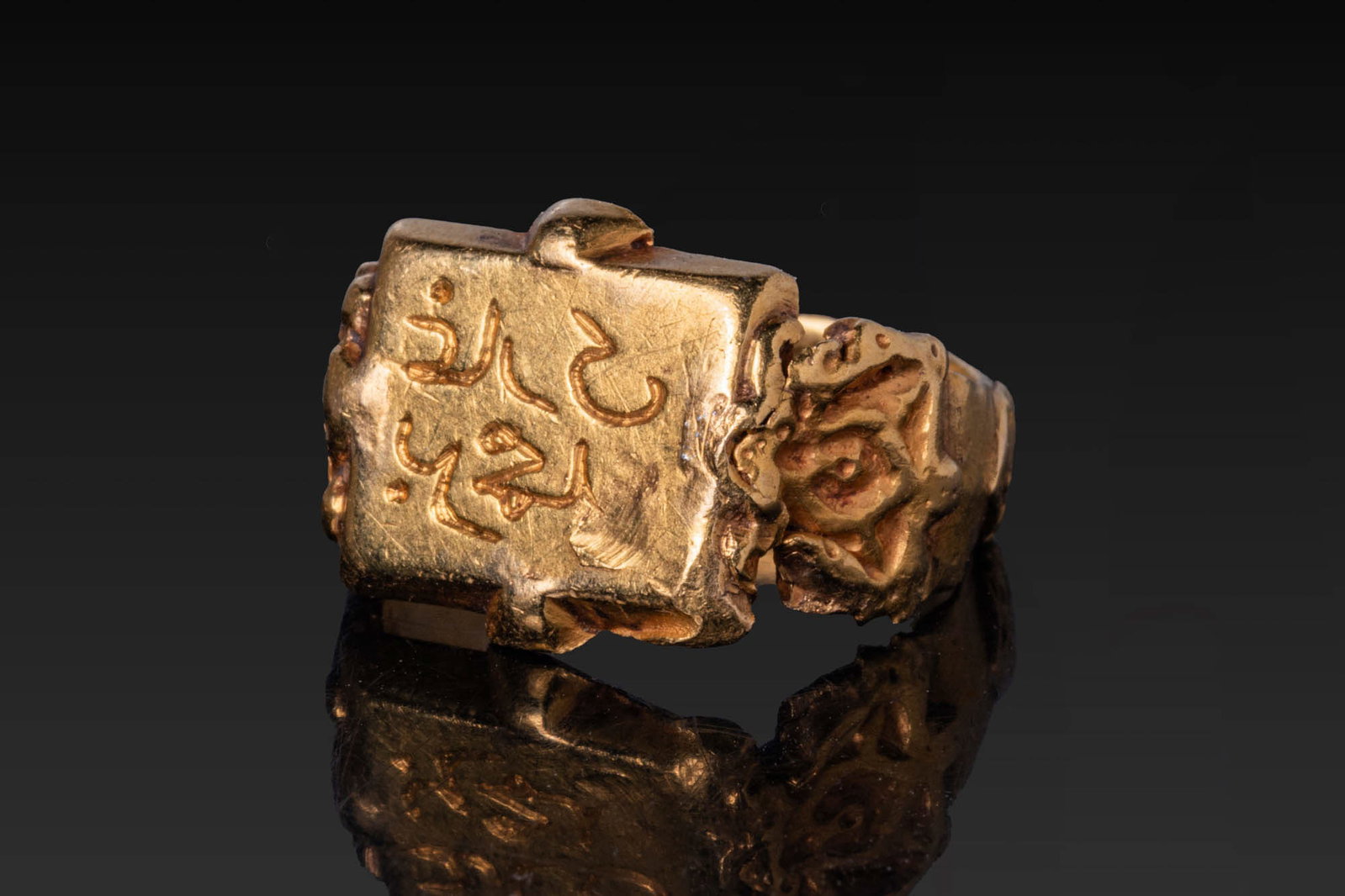 SELJUK SOLID GOLD RING WITH INSCRIPTION: Ca. 13th - 15th century AD. A gold ring with a rectangular bezel framed by a lightly bevelled rim, the field inscribed in neat Kufic script in relief, reading: ??fi? al-?ubb - "Preserver of love." Rob