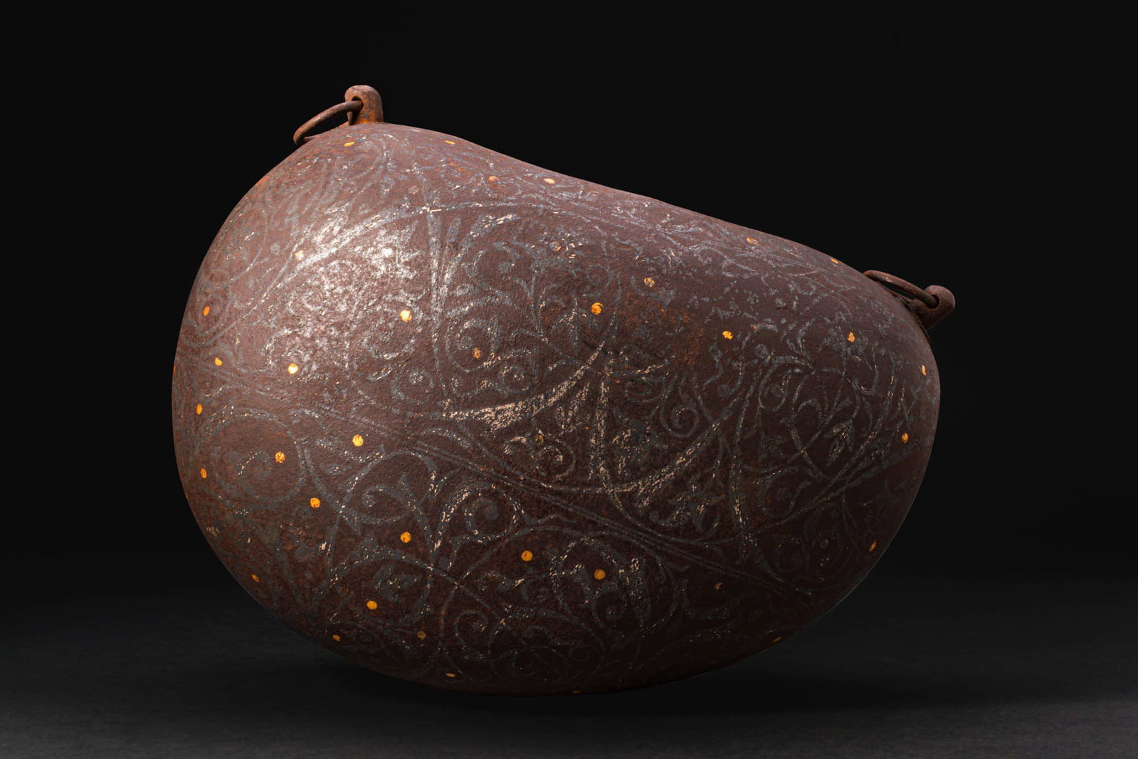 INSCRIBED AND INLAID KASHKUL (BEGGAR'S BOWL): Ca. 19th - 20th century AD. A kashkul of asymmetrical gourd-like form with a broad ovoid mouth set along the upper side. The ends with opposed pierced lugs fitted with loose rings for suspension. The 