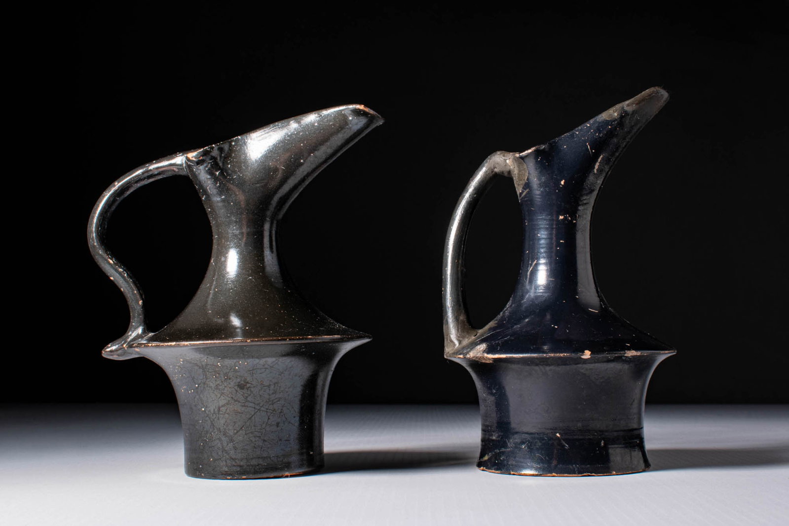 PAIR OF GREEK BLACK GLAZE EPICHYSES: Ca. 350 - 300 BC. A pair of black-glazed epichyses, each with a sharply angled profile and an arching handle extending from the rim to the carinated shoulder. Size: 120-130mm x 80-90mm; Weight: 260g P