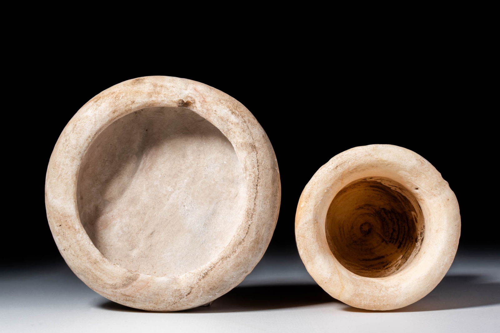 PAIR OF BACTRIAN ALABASTER VESSELS: Ca. 3000 - 2000 BC. A pair of alabaster vessels. The first on the left has a low, rounded profile with a flat base and recessed cavity. The other is a small goblet rising from a disc-shaped base with