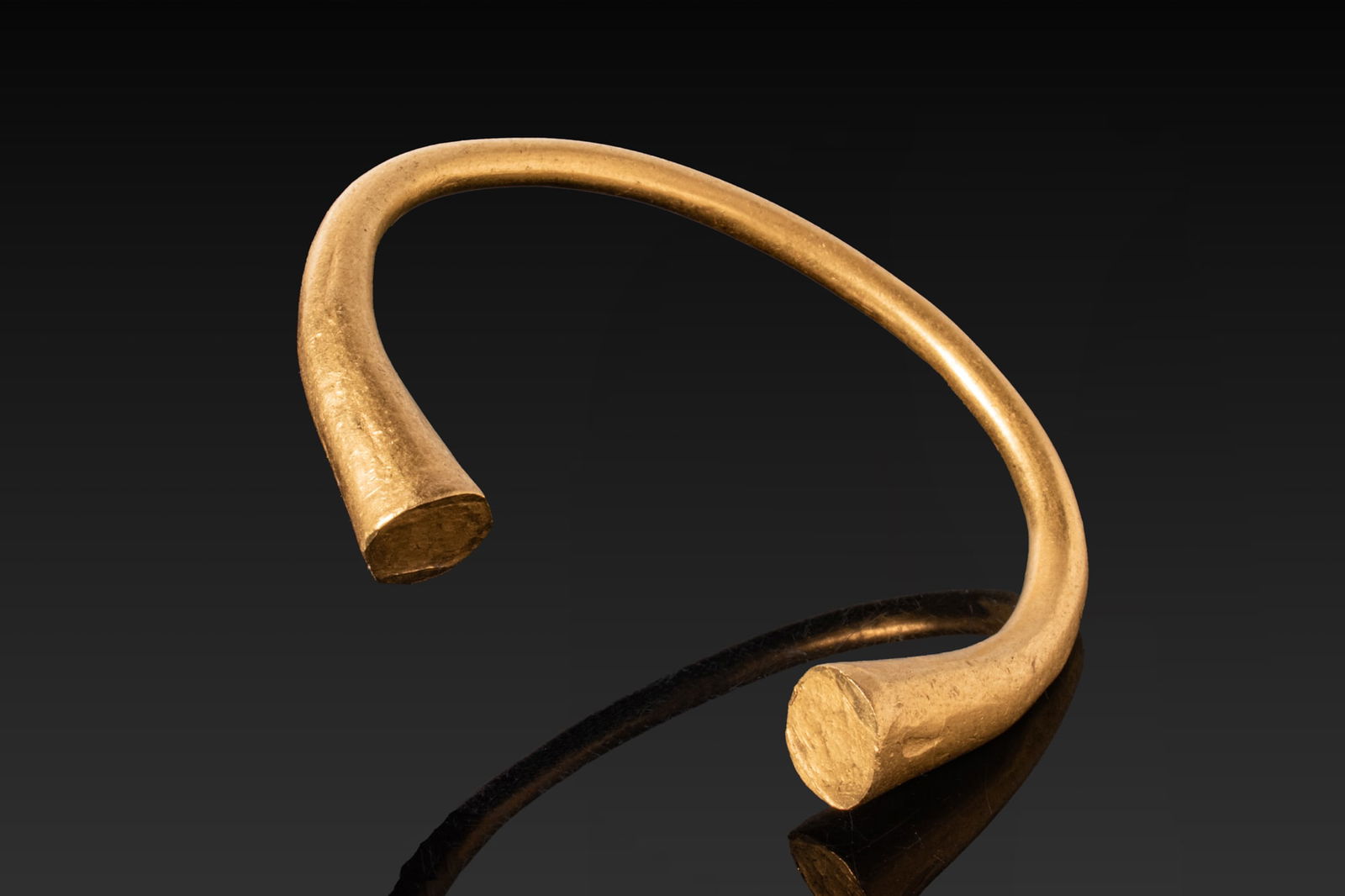VERY HEAVY GREEK SOLID HIGH KARAT 92G GOLD BRACELET: Ca. 500 BC A solid 23.5kt gold penannular bracelet with a thick rounded hoop that gently expands towards the open ends. The terminals flare into broad flattened faces. Size: 75mm x 65mm; Weight: 92g.