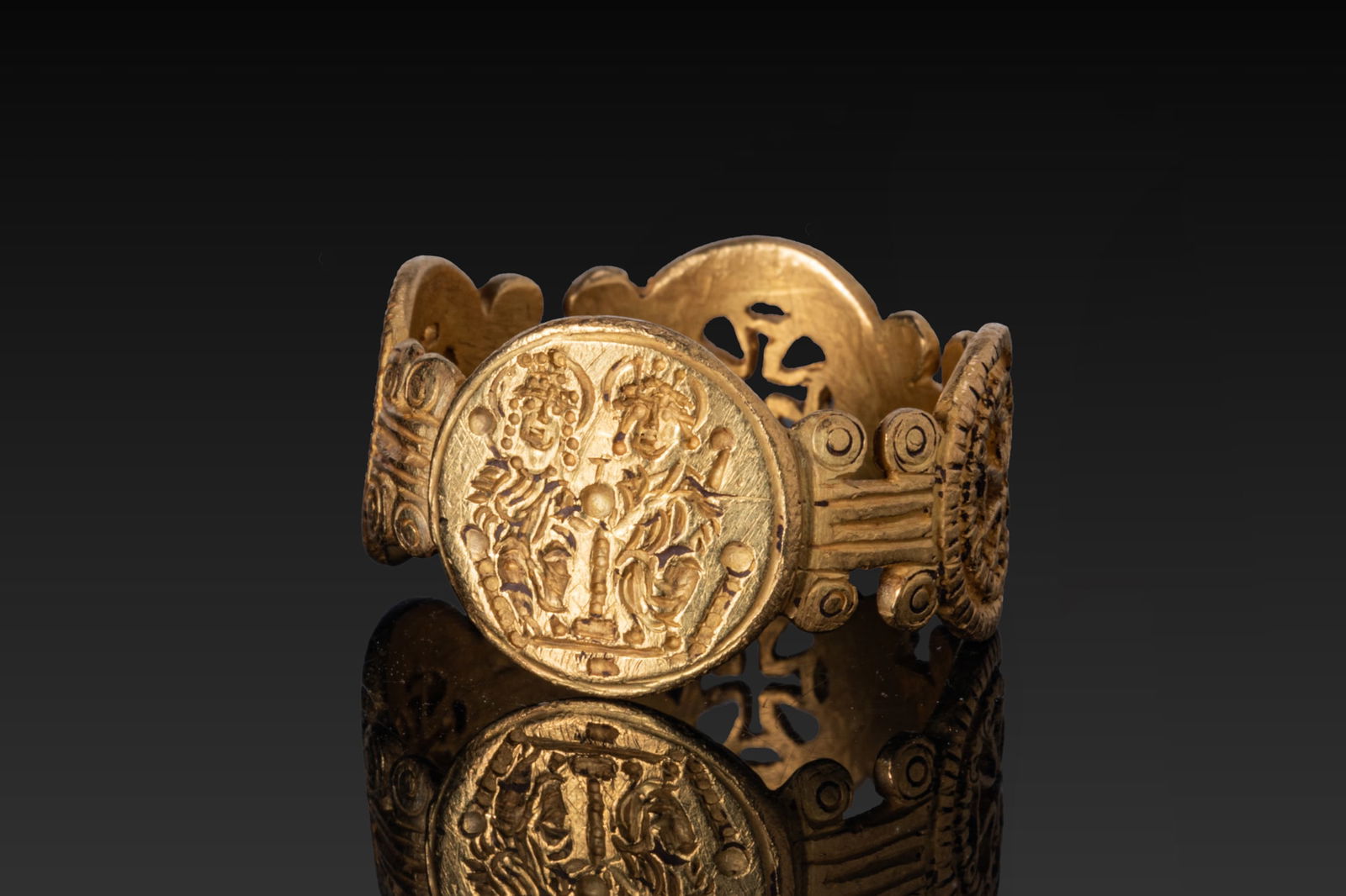 BYZANTINE HIGH KARAT GOLD OPENWORK RING WITH THE IMPERIAL FAMILY: Ca. AD 600 - 700 A gold openwork ring formed as a band of alternating circular medallions linked by short ribbed bars with disc terminals. The main medallion shows in low relief an imperial couple sea