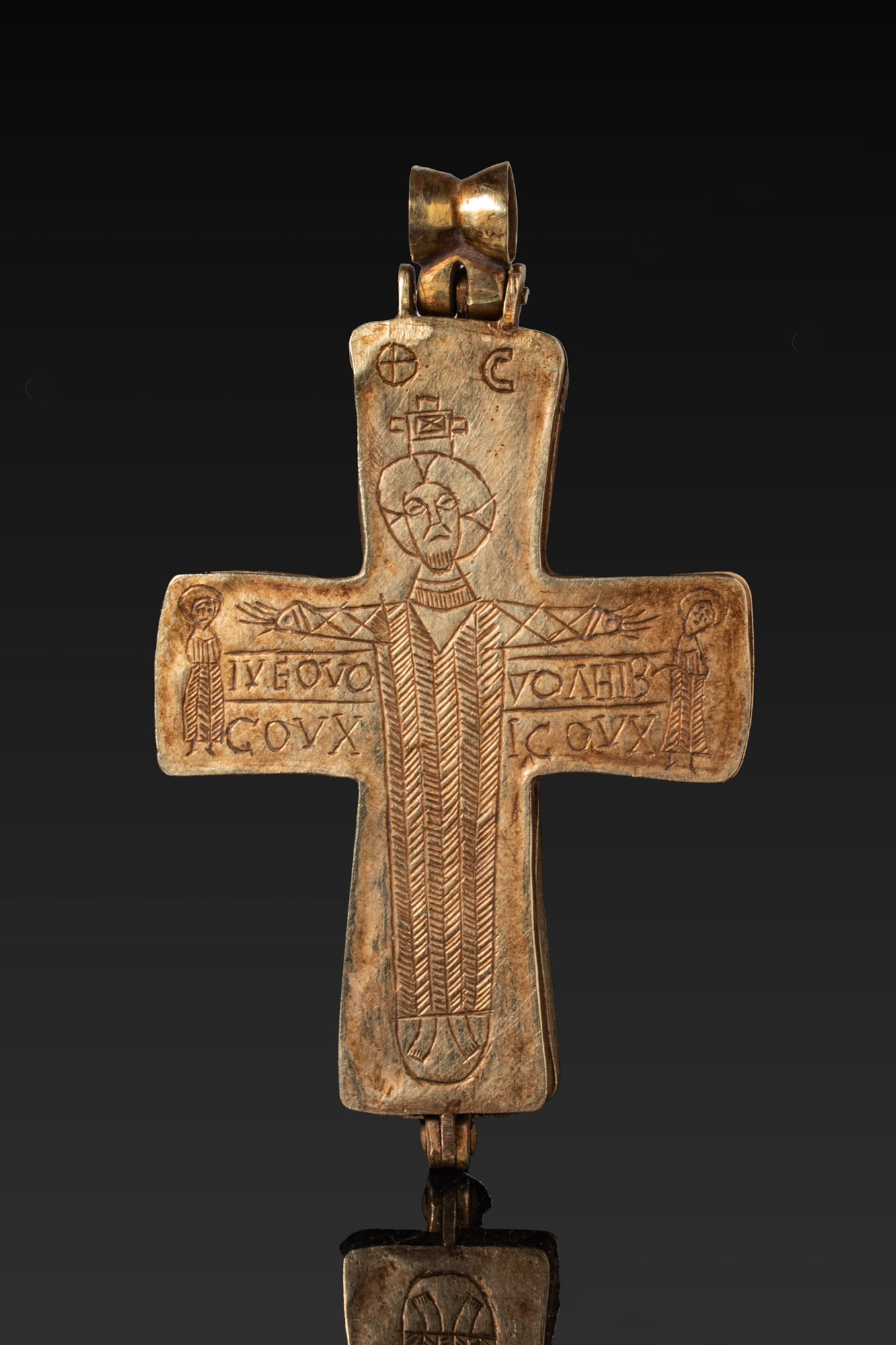 HEAVY BYZANTINE HIGH KARAT GOLD ENKOLPION WITH CRUCIFIXION AND INSCRIPTIONS: Ca. AD 1000 - 1200 A gold enkolpion formed of two hinged cross-shaped plates with a bow-shaped suspension loop on a short mount above the upper arm. The front face is engraved with the Crucifixion, Ch