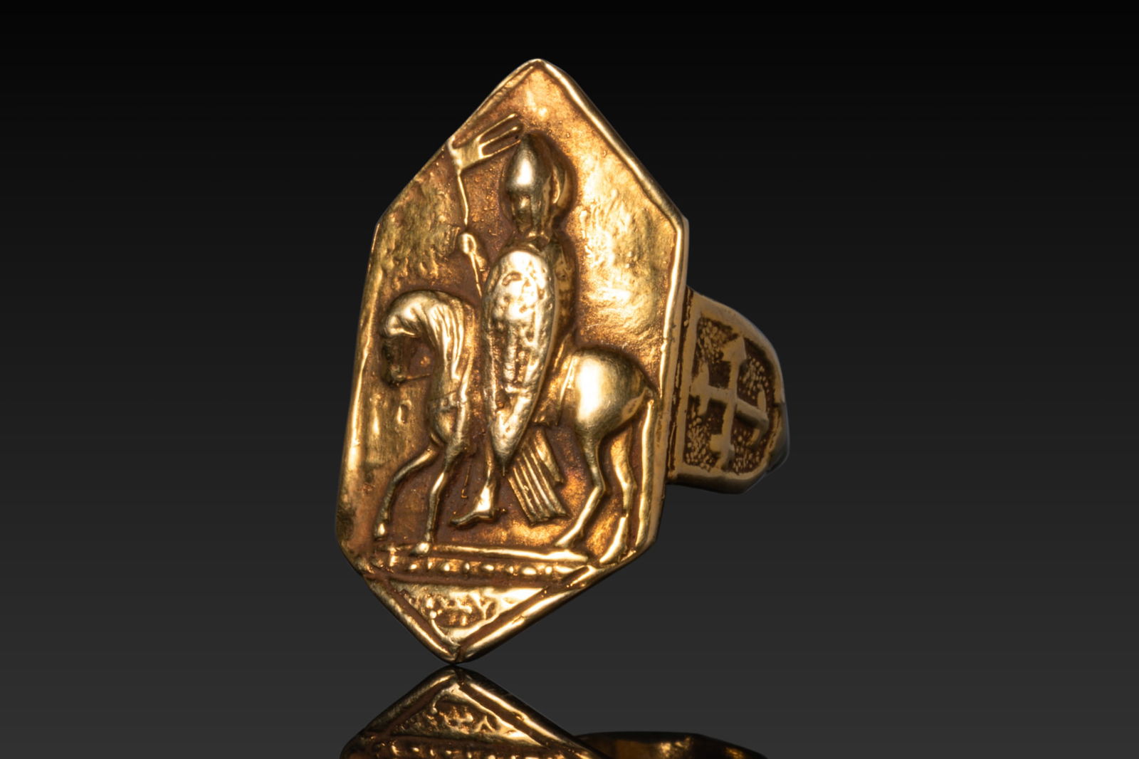 CRUSADER HIGH KARAT GOLD RING WITH ST MAURICE: Ca. AD 1100 - 1300 A gold ring with a flat-section hoop and an elongated bezel decorated in relief with an armoured St Maurice shown in profile, holding a long staff surmounted by a banner and an oval