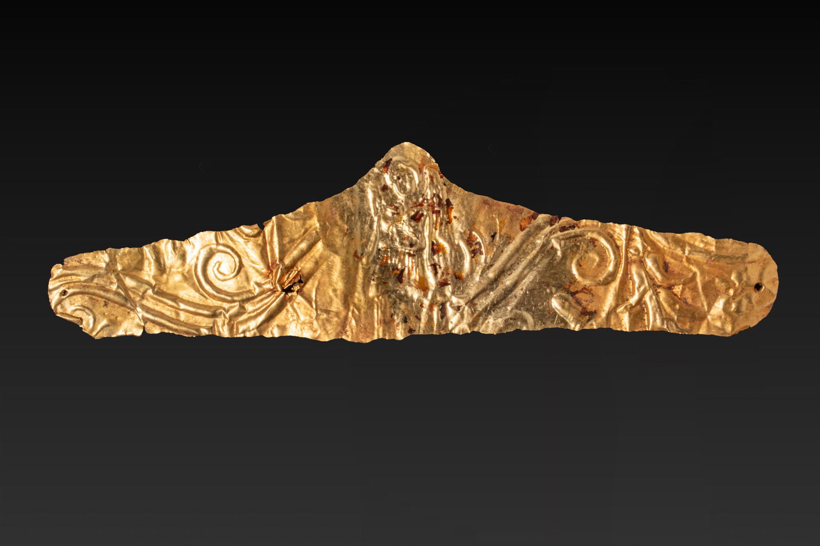 GREEK HIGH KARAT GOLD DIADEM WITH GODDESS AND FLORAL MOTIF: Ca. 350 - 300 BC A gold diadem formed from a thin sheet of gold, with an elongated body and rounded terminals. The band is decorated in repouss? with a central winged Nike standing frontally in a long