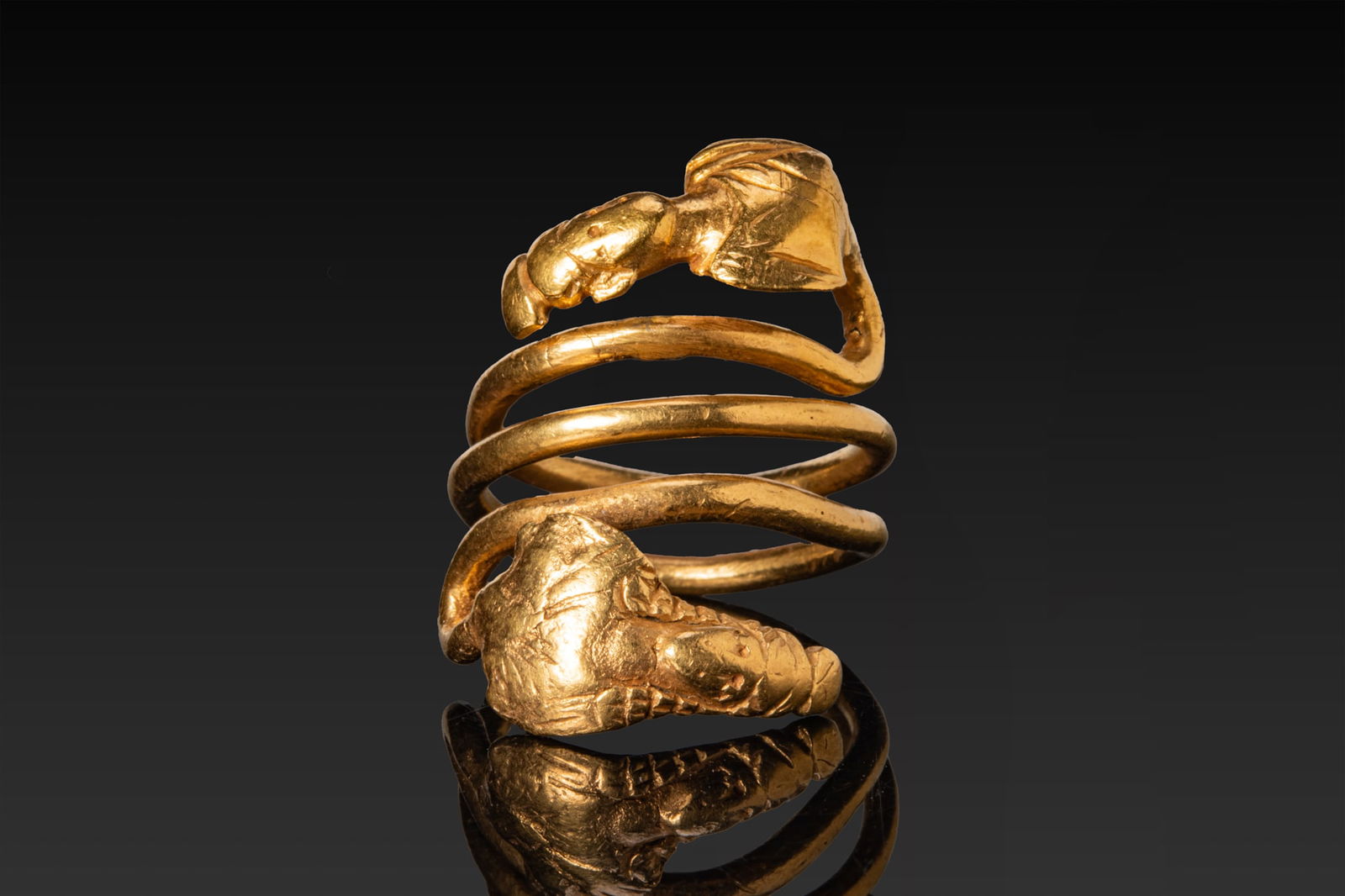 SCARCE ROMAN HIGH KARAT GOLD SPIRAL RING WITH SNAKE-BODIED BUSTS OF ISIS AND SERAPIS: Ca. AD 1 - 100 A fine gold ring made from a round-section wire coiled into a three-turn spiral that terminates in opposed busts. Each end broadens into the modelled head and upper torso of a draped de