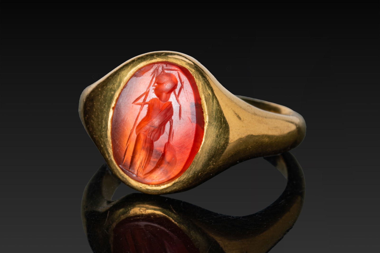 ROMAN CARNELIAN INTAGLIO WITH MINERVA IN GOLD RING: Ca. AD 50 - 200 A carnelian intaglio engraved with Minerva standing in profile, helmeted and draped, holding a long spear and a round shield at her side, the stone mounted in a possibly later gold fin
