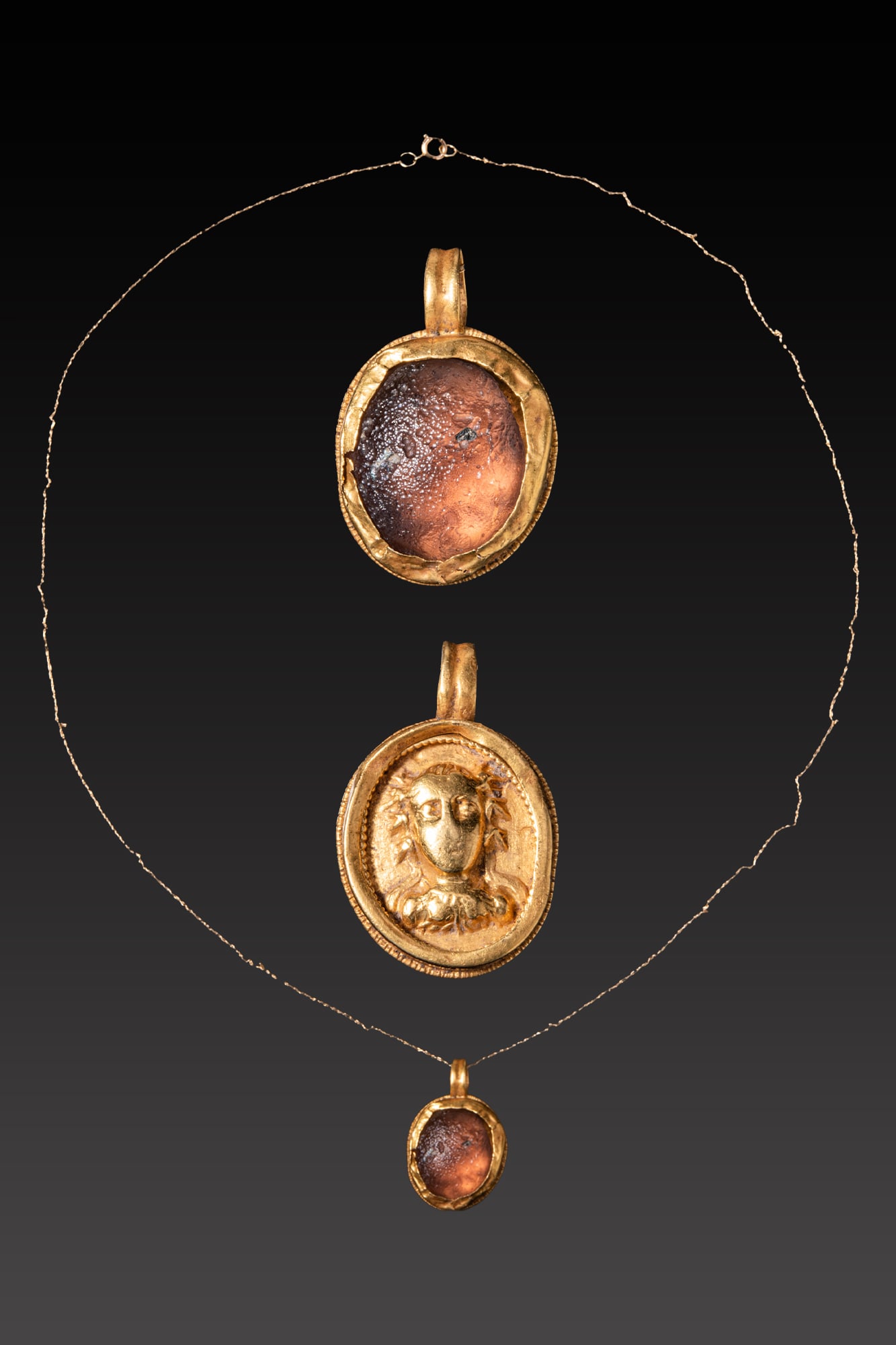 ROMAN GOLD NECKLACE WITH GLASS GEM AND YOUNG BACCHUS: Ca. AD 1 - 300 A gold necklace composed of a fine chain suspending an oval pendant. On one side the pendant is set with a convex glass insert within a plain gold frame; on the reverse an oval medallio