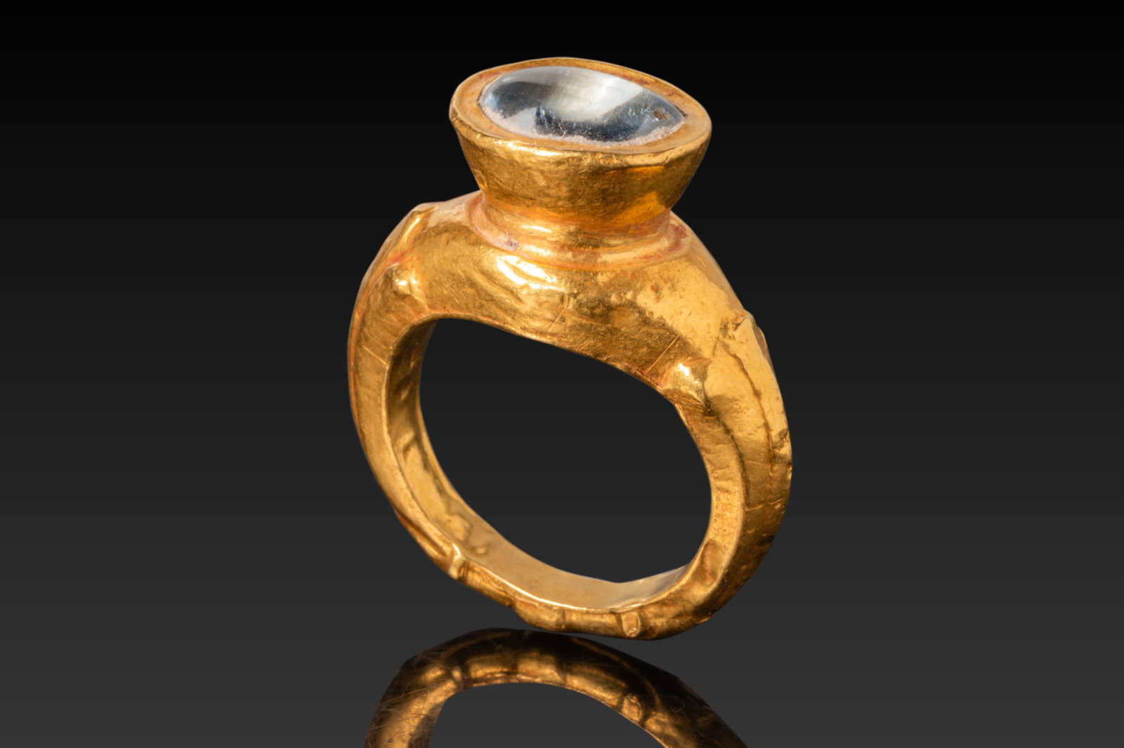 LATE ROMAN HIGH KARAT GOLD RING WITH AQUAMARINE: Ca. AD 200 - 300 A gold ring formed from a hoop of near-rectangular section, narrow at the back and broadening into faceted shoulders that support a tall circular cell set with an aquamarine cabochon.