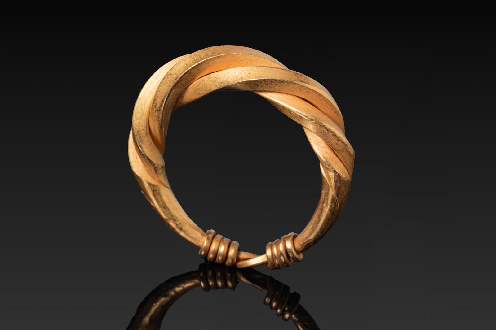 VIKING HIGH KARAT GOLD TWISTED RING: Ca. AD 900 - 1100 A gold ring with a hoop formed from three broad rods twisted together, the twisted section merging on each side into a plain round-section hoop finished with tightly coiled wire coll