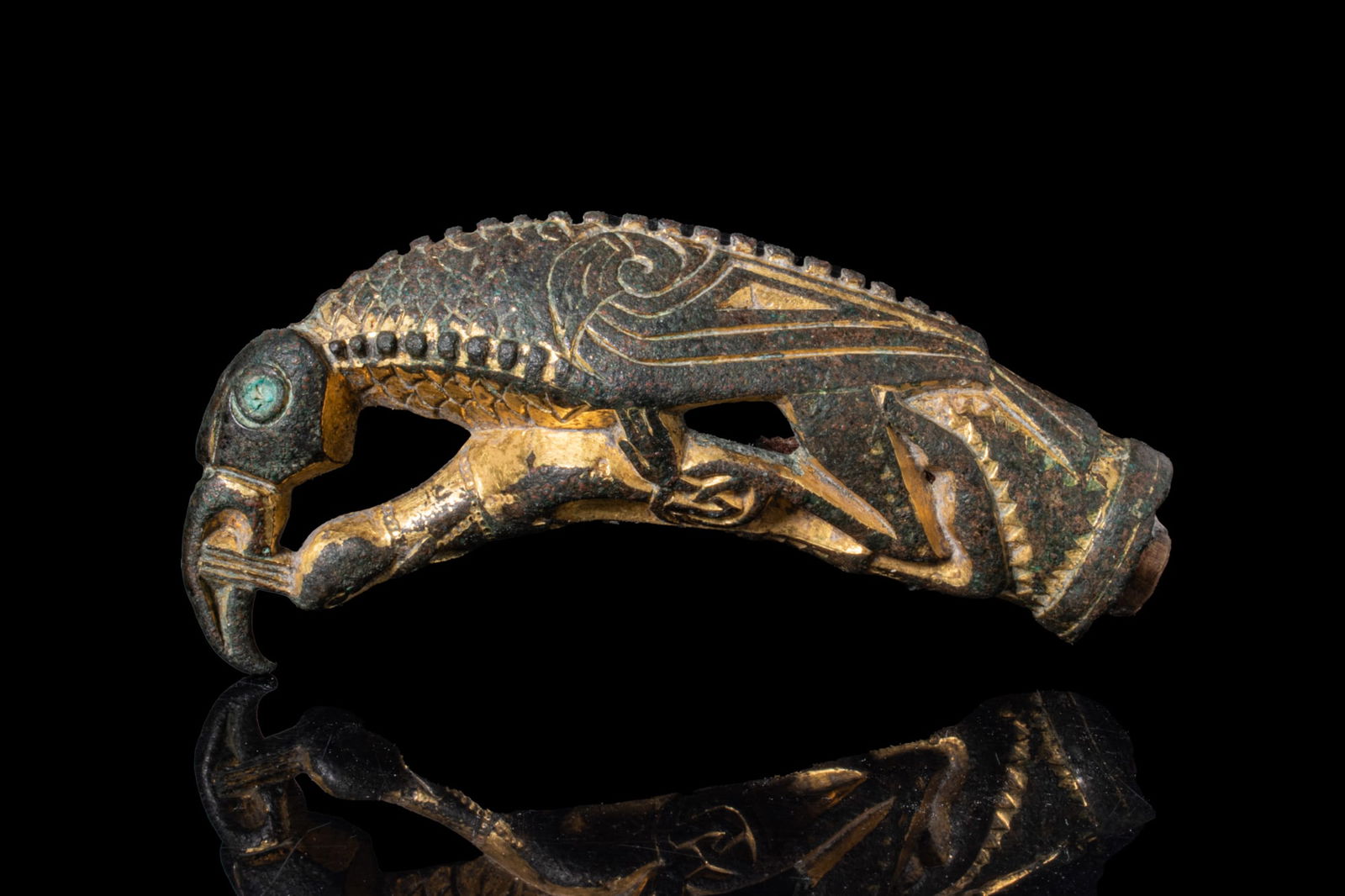 VIKING GILT-BRONZE RAVEN FIGURINE: Ca. AD 800 - 1000A gilt-bronze raven figurine modelled with an arched neck and hooked beak, the head with a large circular eye in green inlay. The back is decorated with a central ridge and rows of bo