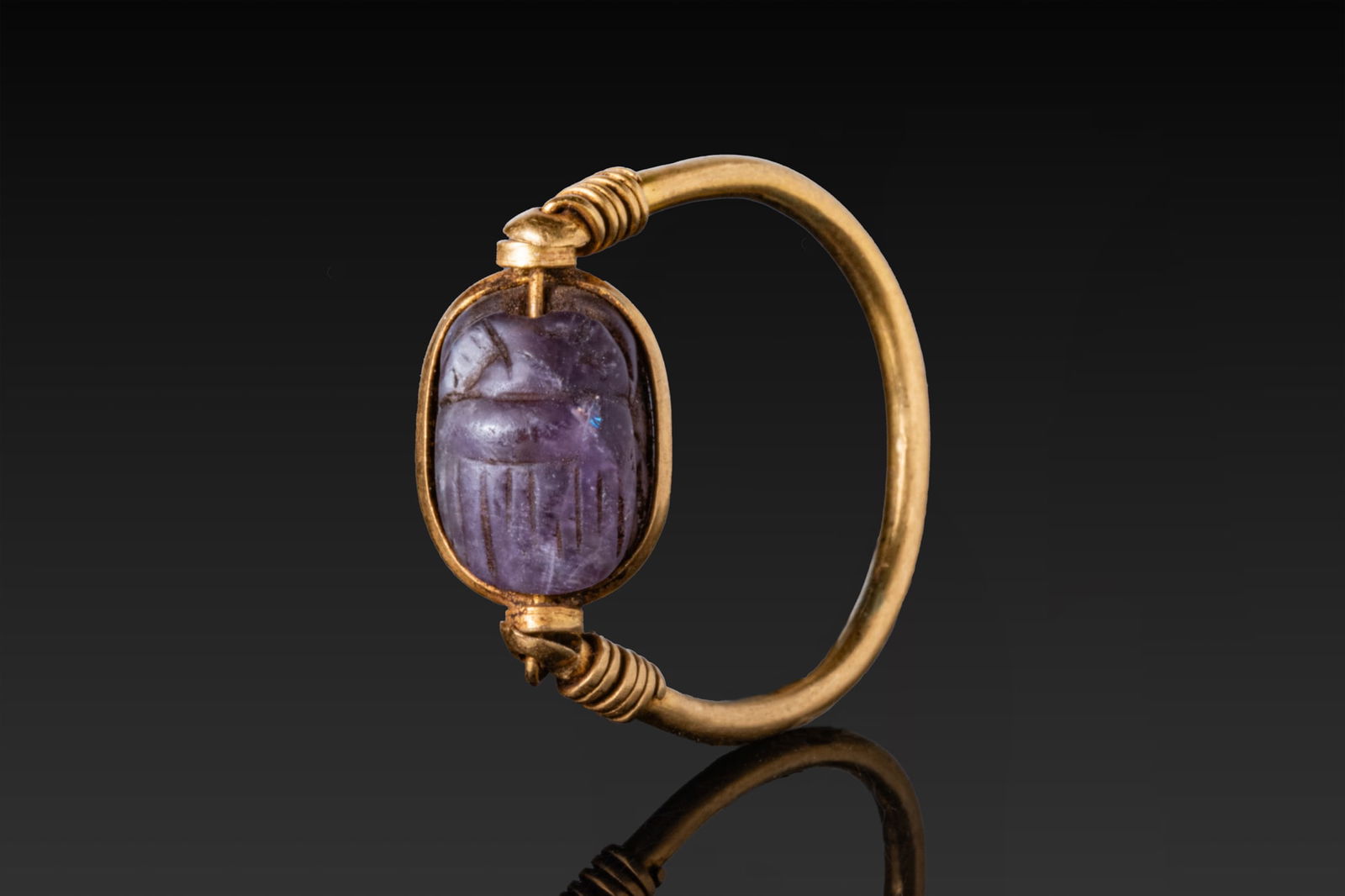EGYPTIAN AMETHYST SCARAB IN GOLD SWIVEL RING: Late Period, Ca. 664 - 332 BCAn amethyst scarab carved with a rounded head, convex pronotum and elytra with vertical ribbing, the flat underside engraved with hieroglyphic signs, and mounted in an ova