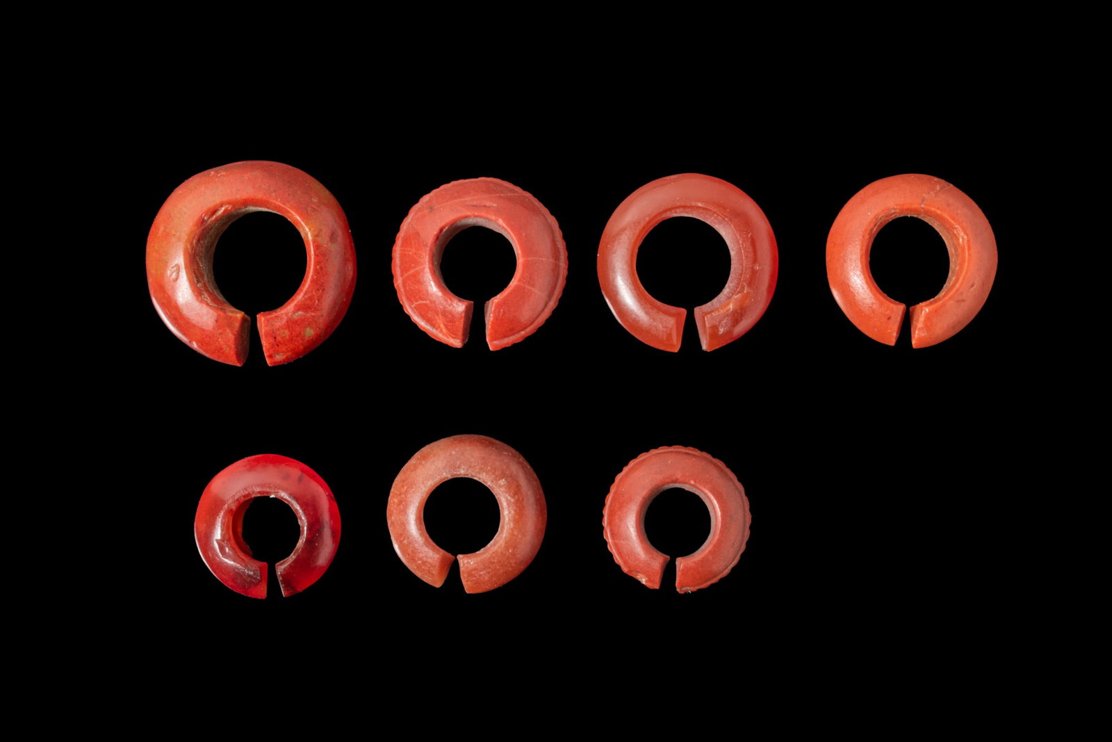 COLLECTION OF EGYPTIAN JASPER AND CARNELIAN EARRINGS OR HAIR RINGS - EX CHRISTIE'S: New Kingdom, Ca. 1550 - 1069 BCA collection of seven red jasper and carnelian earrings or hair rings, each formed as a thick penannular hoop with a transverse opening and a broad cylindrical interior,