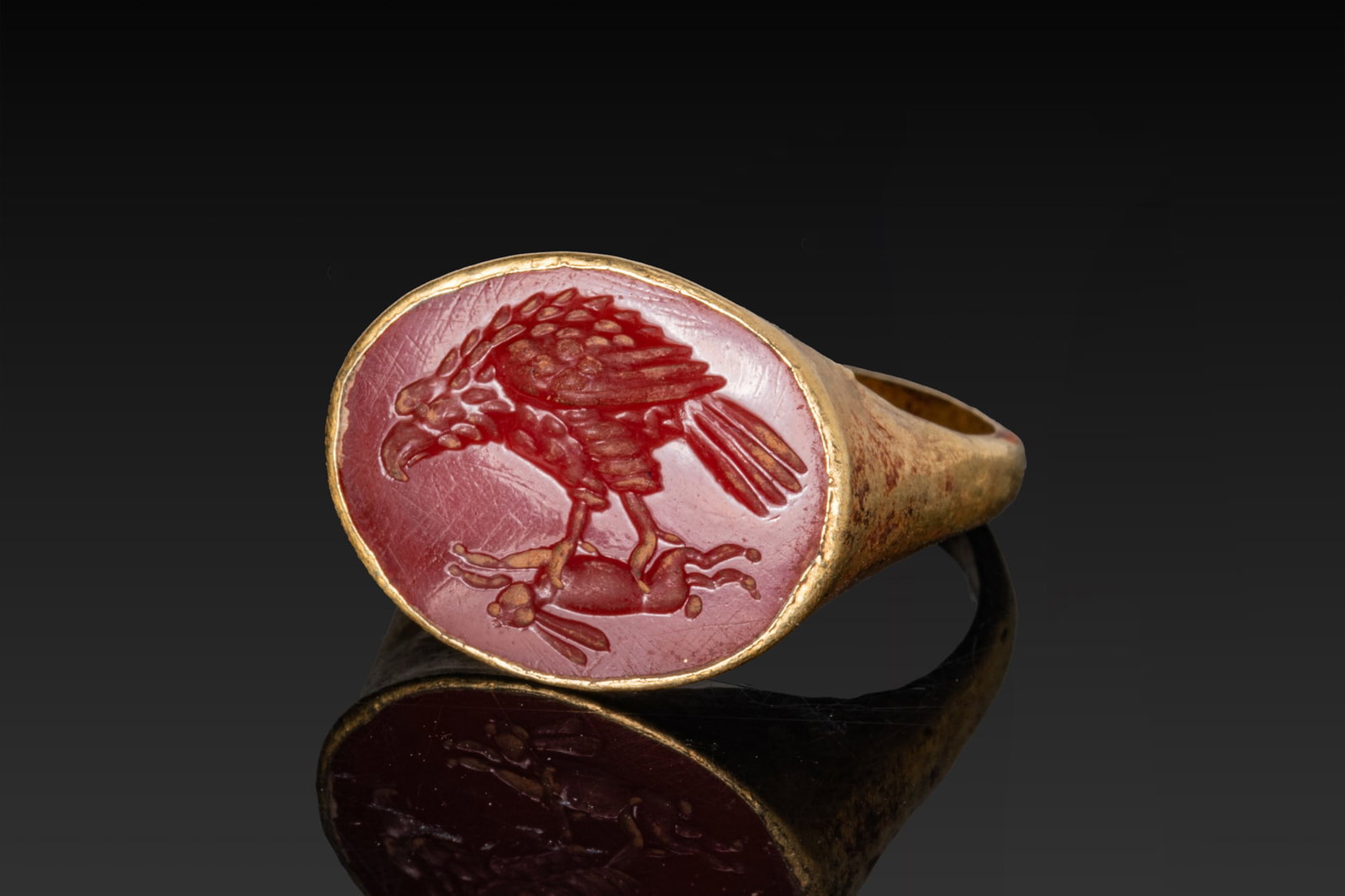 ROMAN GOLD RING WITH CARNELIAN INTAGLIO OF AN EAGLE GRASPING A HARE: Ca. AD 1 - 300A gold ring with a broad oval bezel plate rising from sloping shoulders above a rounded hoop. The bezel encloses a carnelian intaglio engraved with an eagle in profile to left, the pluma