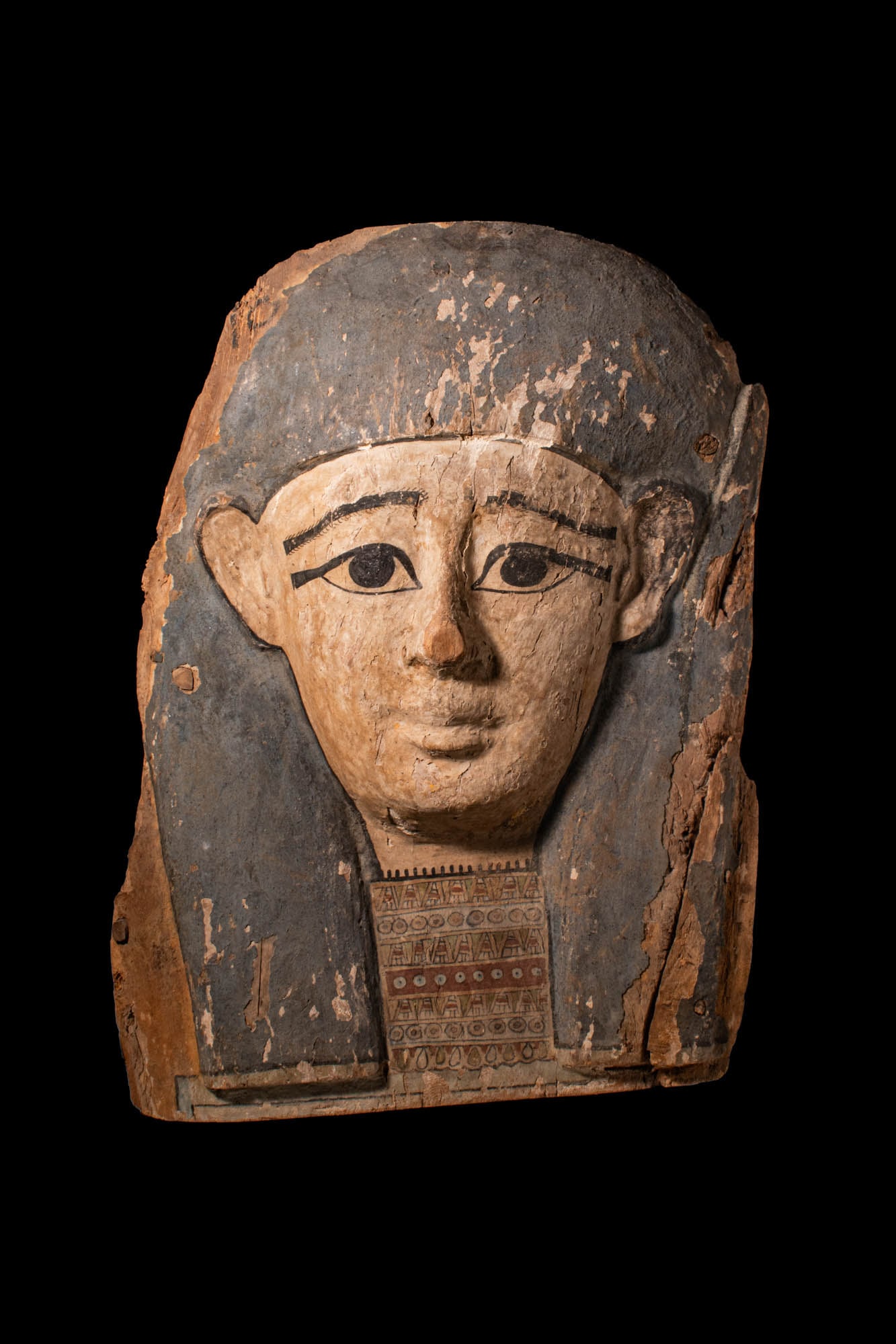 LARGE EGYPTIAN PAINTED SARCOPHAGUS PANEL WITH MASK: Late Period to Ptolemaic Period, Ca. 664 - 30 BC. A carved wooden sarcophagus panel with a mask with painted detail, depicting a stylised face with large, almond-shaped eyes outlined in black, arched