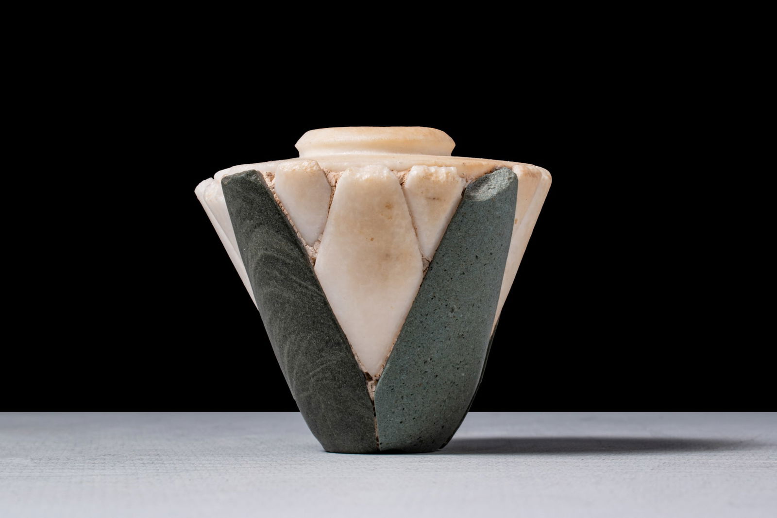 EGYPTIAN MULTI STONE LOTUS CUP: Late Predynastic Period to Early Dynastic Period, Ca. 3325 - 2575 BCA travertine and argillite vessel in the form of a lotus flower, with a tapering body rising to a flat shoulder and a short