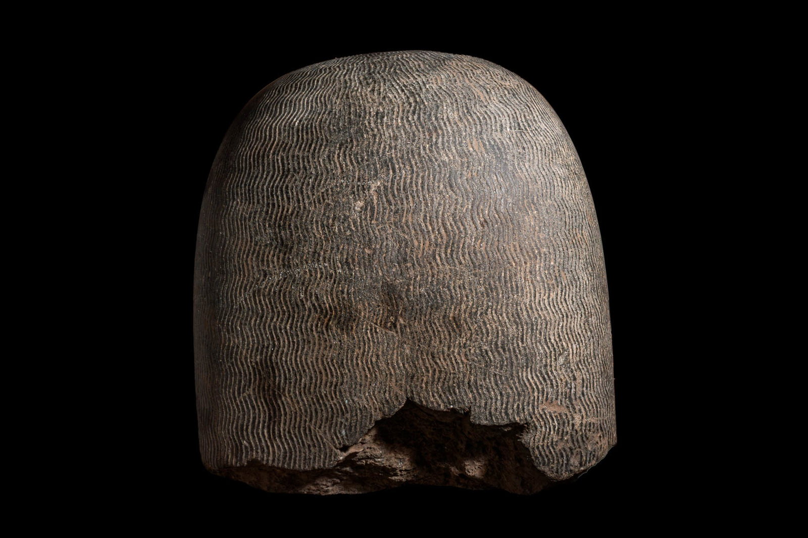 COLOSSAL EGYPTIAN FRAGMENTARY STONE HEAD OF COLOSSAL STATUE: New Kingdom, Ca. 1550 - 1069 BC. A large fragment from the back of a colossal head in dark hardstone, the surface carved with tightly spaced, horizontally arranged undulating ridges representing the
