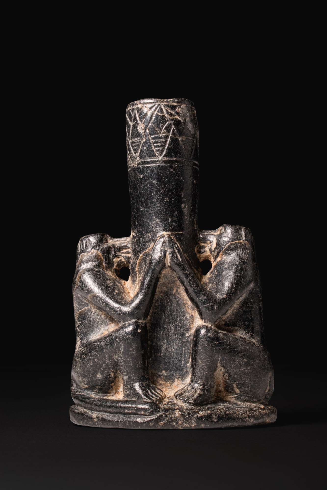 EGYPTIAN BLACK STONE KOHL TUBE WITH BABOONS: Late Period, Ca. 664 - 332 BCA black stone kohl tube formed as a vertical cylindrical container rising from an oval base. The sides are flanked by a pair of seated baboons carved in the round, each wi