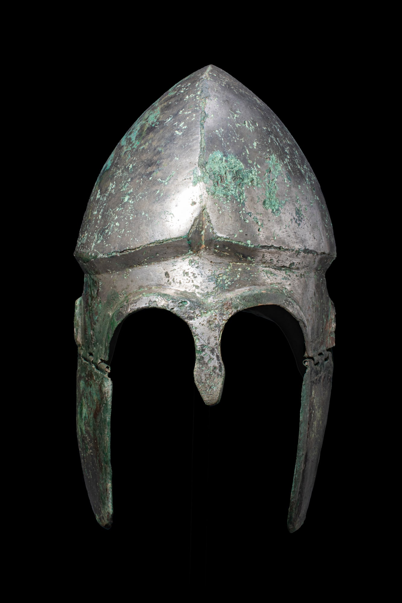 CHALCIDIAN HIGH TIN BRONZE HELMET WITH CHEEKS: Ca. 300 BCA bronze Chalcidian helmet with a domed crown and a prominent horizontal ridge encircling the lower section. The front has arched openings for the eyes, separated by a short, projecting