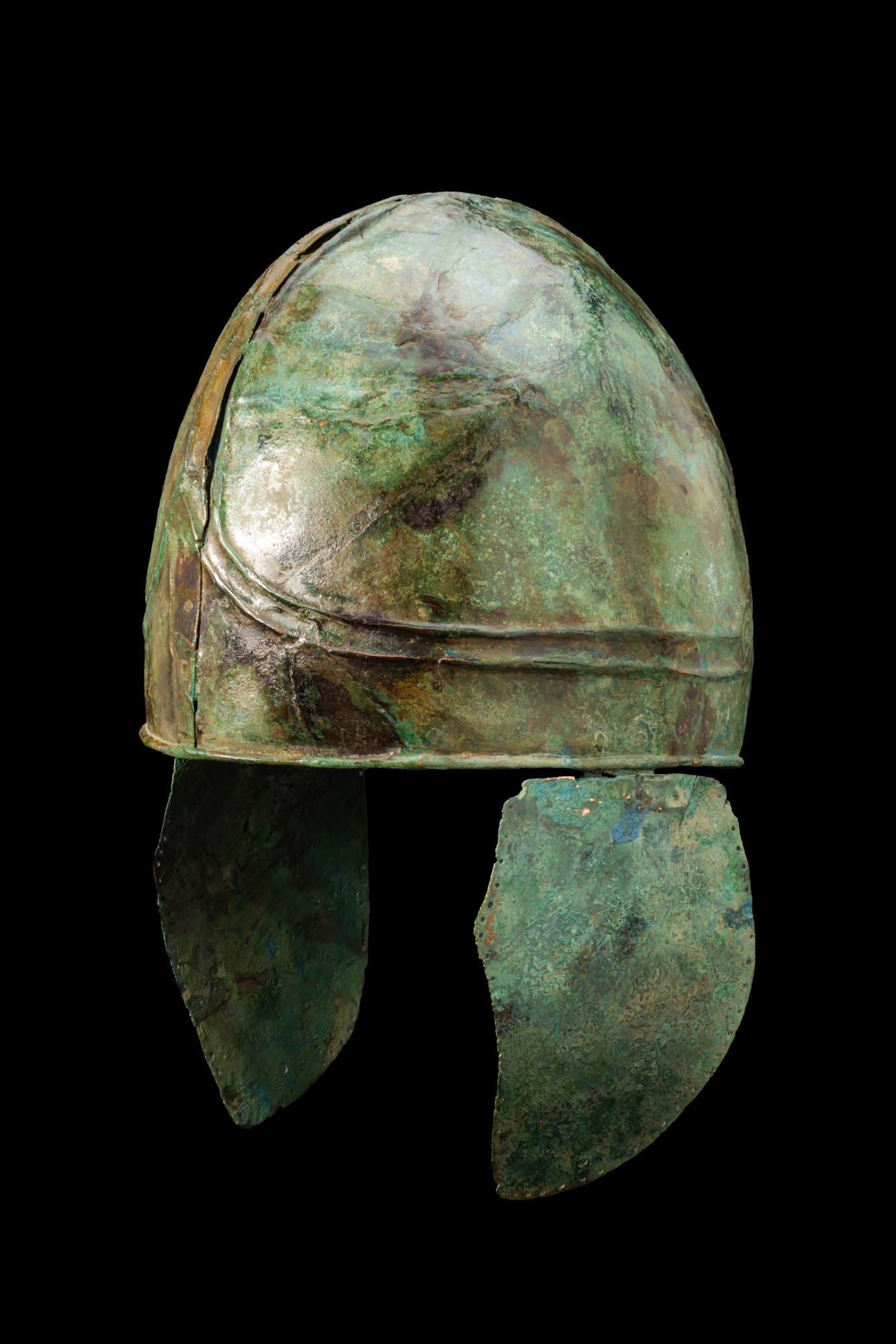 CHALCIDIAN / ATTIC BRONZE HELMET WITH CHEEKPIECES: Ca. 300 - 200 BC A bronze helmet of Chalcidian type with a high ovoid skull surmounted by three longitudinal ribs that run over the crown and diverge into a V-shape above the brow. From this point,