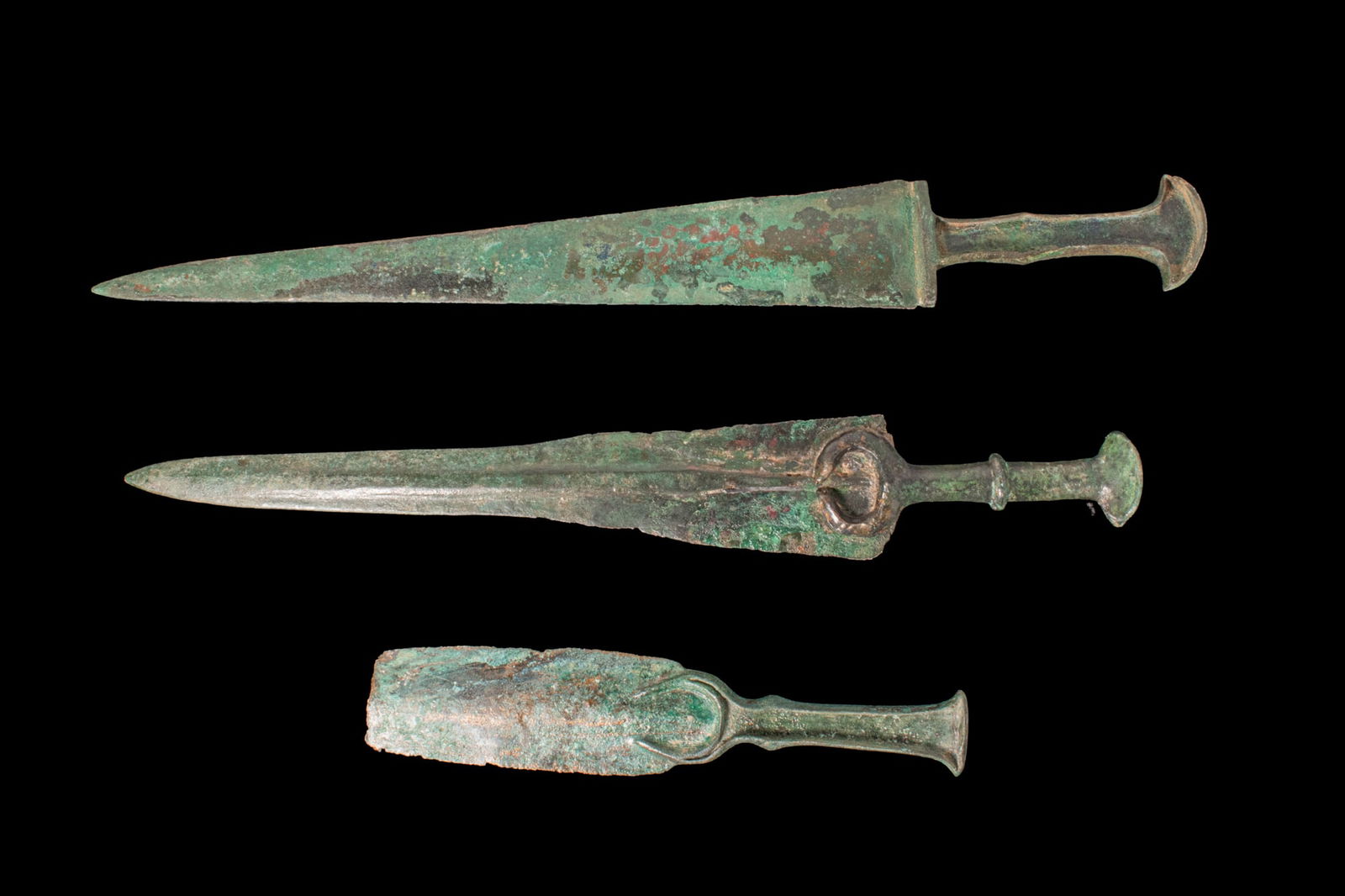 COLLECTION OF BRONZE AGE / EARLY GREEK PERIOD BRONZE DAGGER BLADES: Ca. 1100 - 800 BCA collection of three bronze blades, including, from top to bottom: a long double-edged dagger with elongated triangular blade descending to a flanged recessed hilt for inlay and a