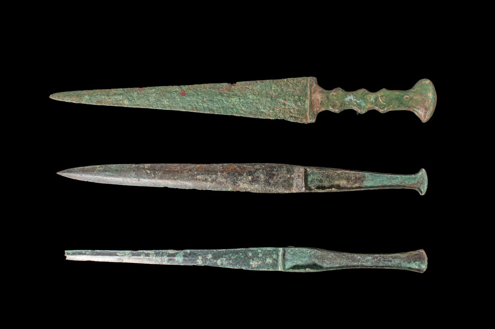 COLLECTION OF BRONZE AGE / EARLY GREEK PERIOD BRONZE DAGGERS: Ca. 1100 - 800 BCA collection of three bronze daggers, including, from top to bottom: a long, narrow, double-edged dagger of triangular profile tapering to a sharp point, the shoulders leading to an