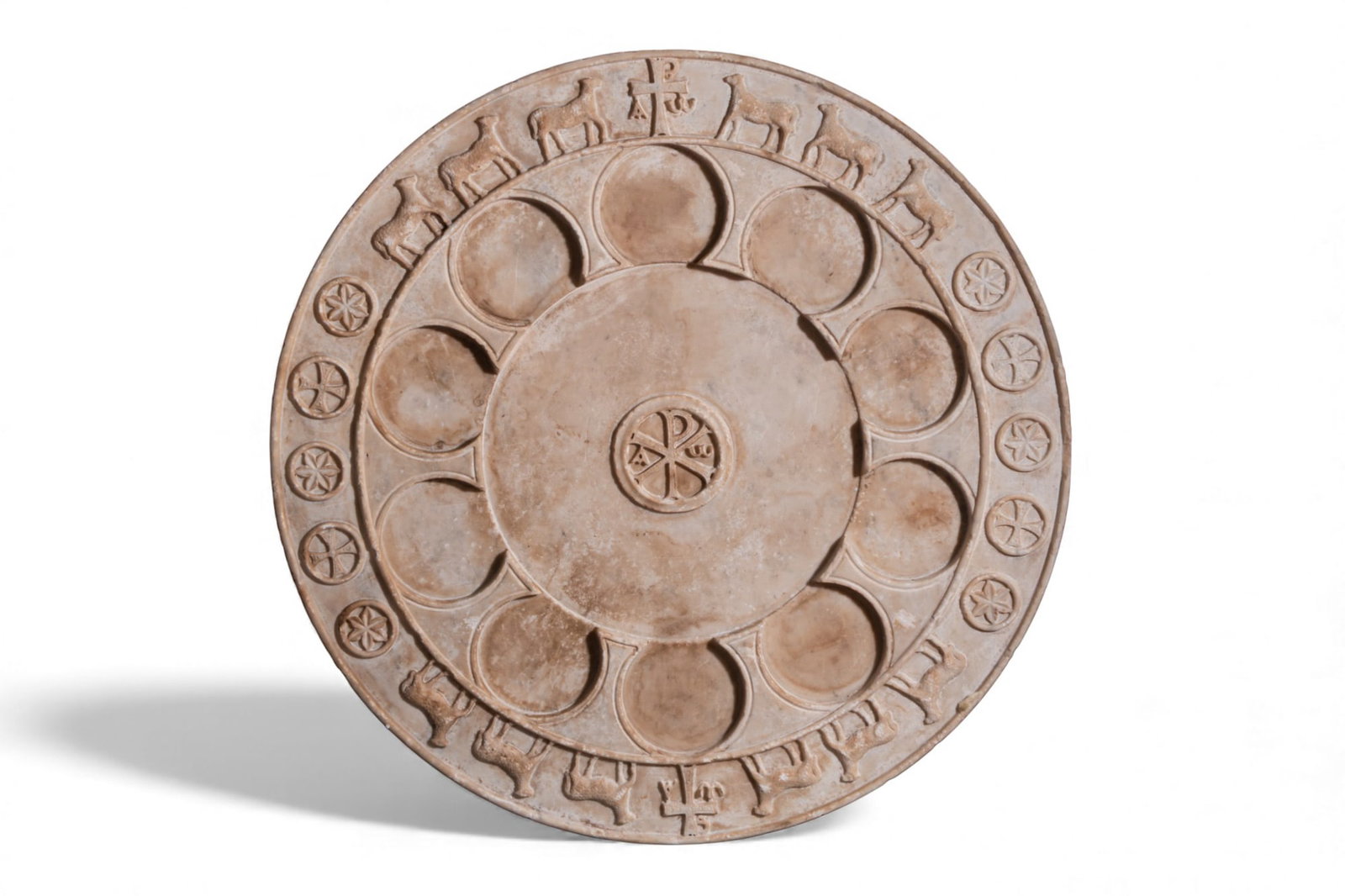 BYZANTINE MARBLE TABLE TOP WITH CHI-RHO AND AGNUS DEI: Ca. AD 600 - 800 A circular marble table top carved as a thick disc with a slightly raised rim and a face decorated with concentric registers. At the centre is a roundel enclosing a Chi-Rho monogram b