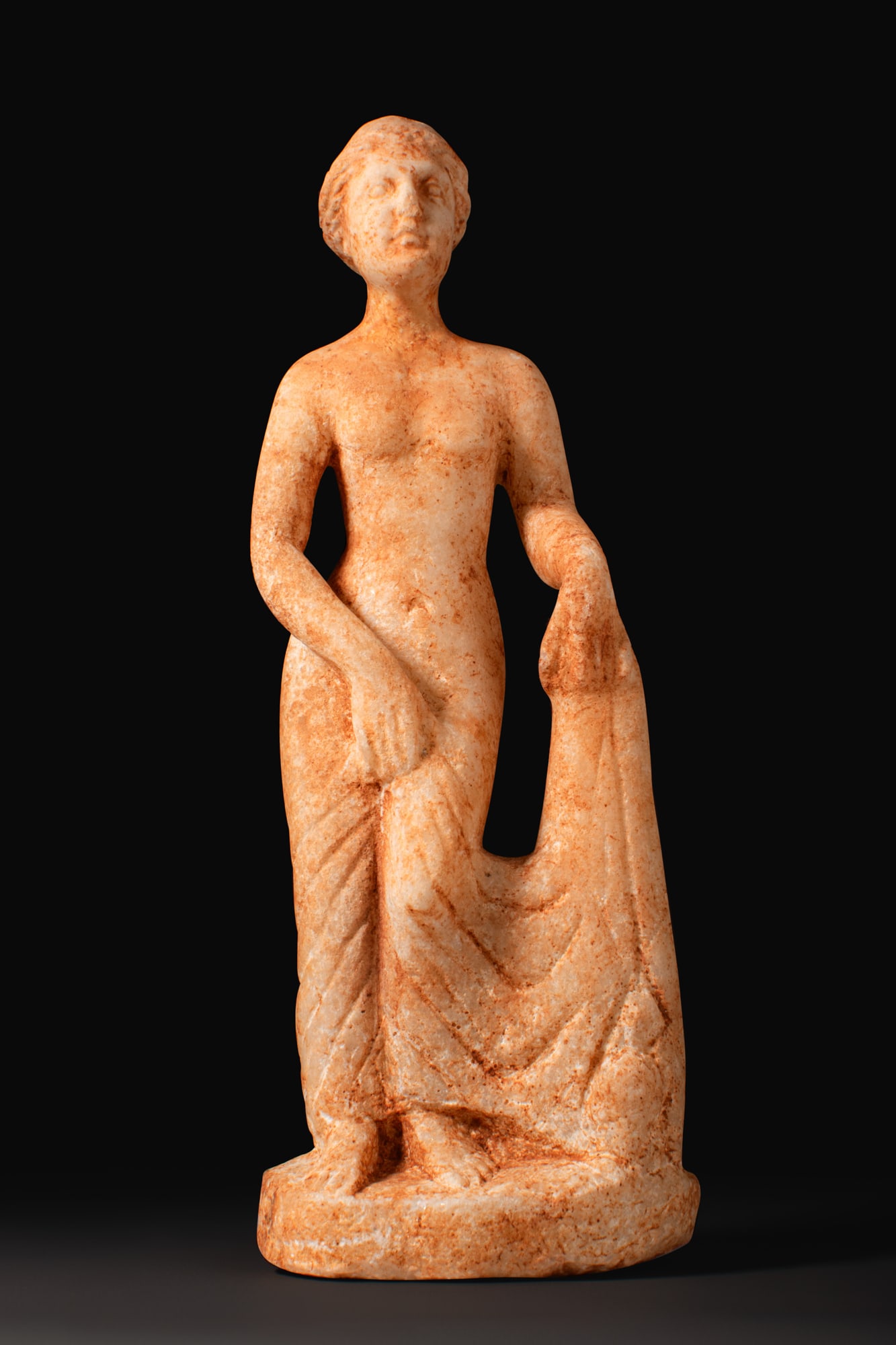 ROMAN MARBLE VENUS FIGURE: Ca. AD 300 - 400A marble figure of Venus standing nude on an integral oval base, her weight on the right leg with the left slightly advanced, the right arm drawn across the torso with the hand reachin