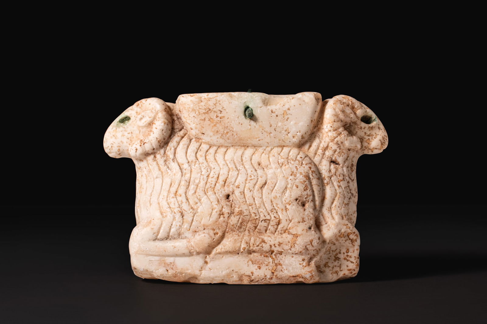 SUMERIAN MARBLE COMPARTMENTED VESSEL SUPPORTED BY RAMS: Ca. 2600 - 2500 BCA marble compartmented vessel supported by a pair of recumbent rams carved back to back, the rectangular upper container cut with two circular cavities and small circular perforation