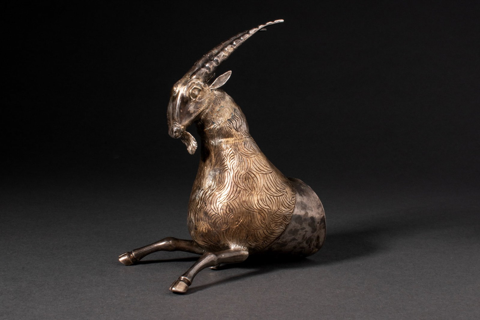 EASTERN GREEK SILVER STAG PROTOME: Ca. 500 BC or later A silver stag protome modelled in the round with a hollow body and forelegs extended forward. A long arched neck supports a narrow head with pointed ears, prominent eyes, and a sma