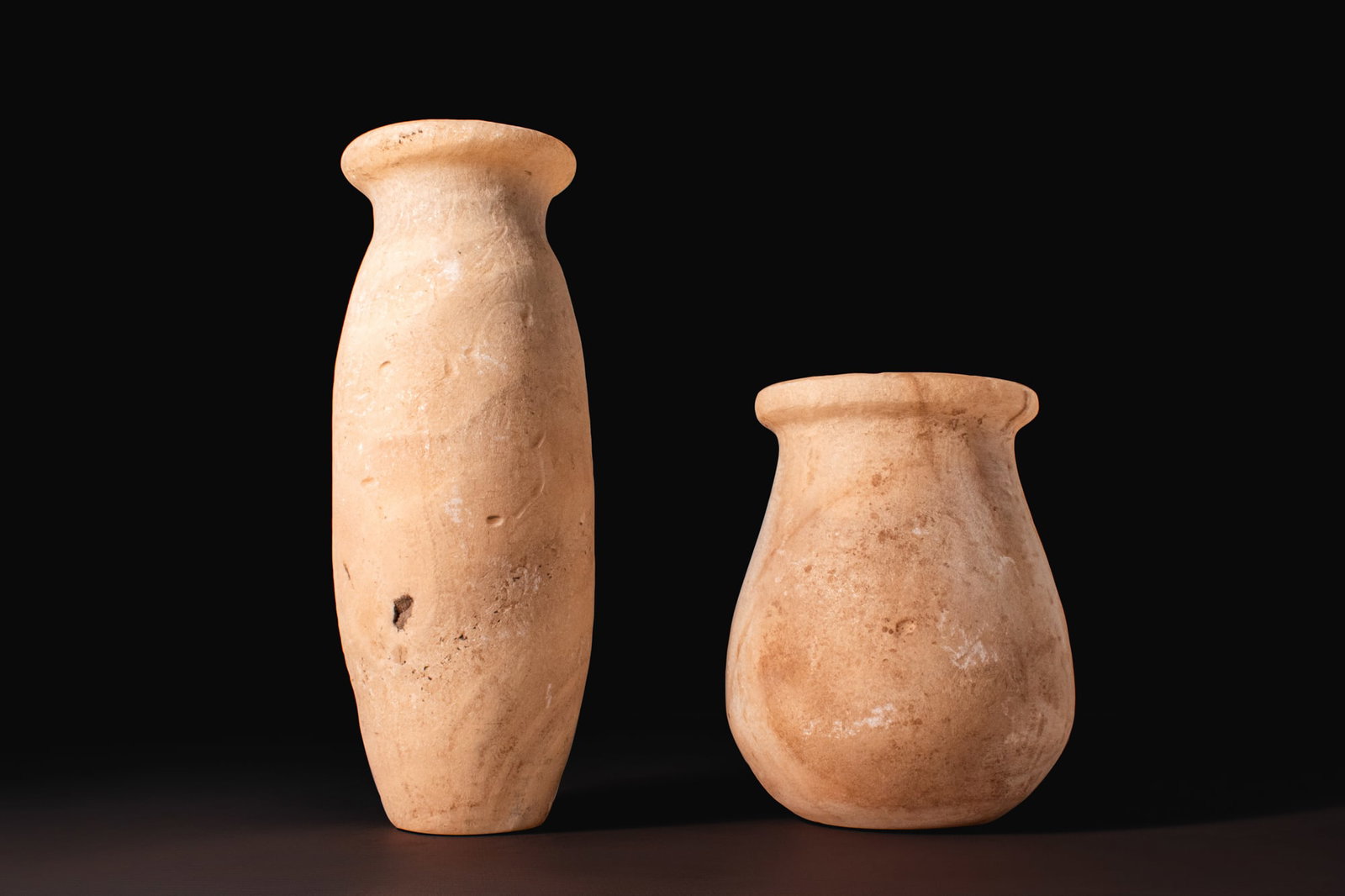 PAIR OF EGYPTIAN STONE VESSELS: Old Kingdom, Ca. 2640 - 2200 BCA pair of alabaster vessels, including, from left to right: a tall cylindrical jar with slightly tapering sides, a flat base, and pronounced rim; and a squat ovoid jar