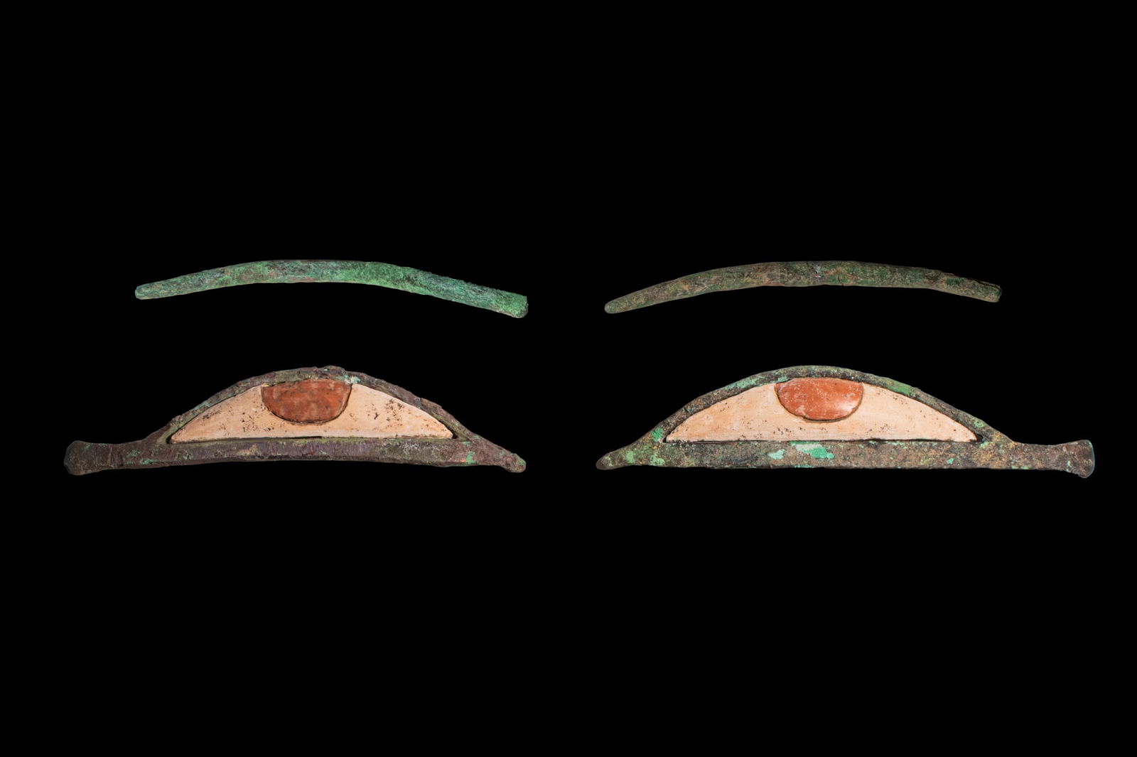 PAIR OF EGYPTIAN BRONZE AND STONE INLAID EYES: Late Period, Ca. 664 - 332 BCA pair of inlaid eyes composed of bronze almond-shaped frames, each set with a cream stone sclera and a reddish stone iris. The bronze lids taper to pointed outer corners